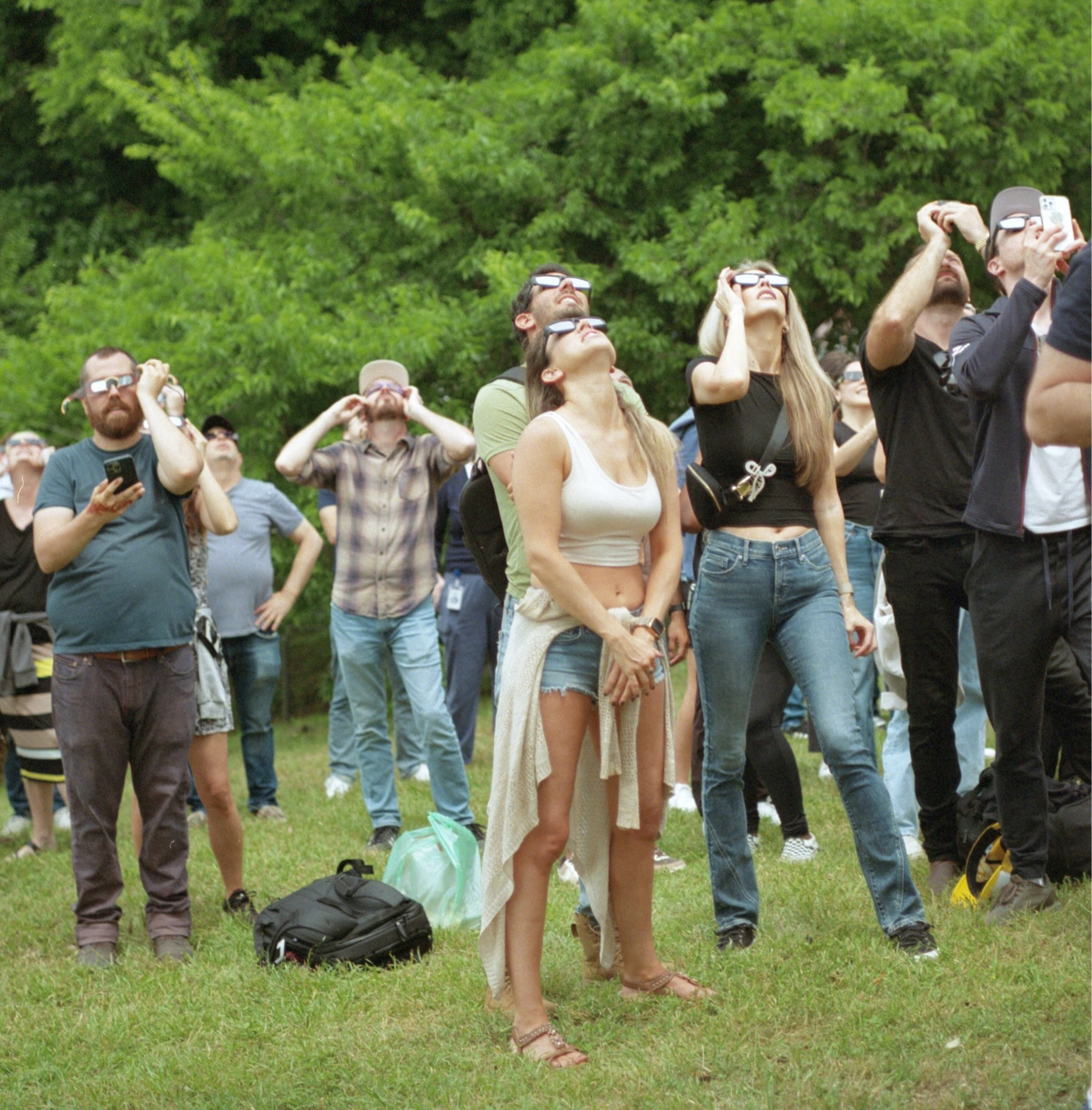 A colour film photo. A group of people who are wearing their eclipse glasses look skyward for the start of the solar eclipse in downtown Austin, Texas. Monday, April 8, 2024.