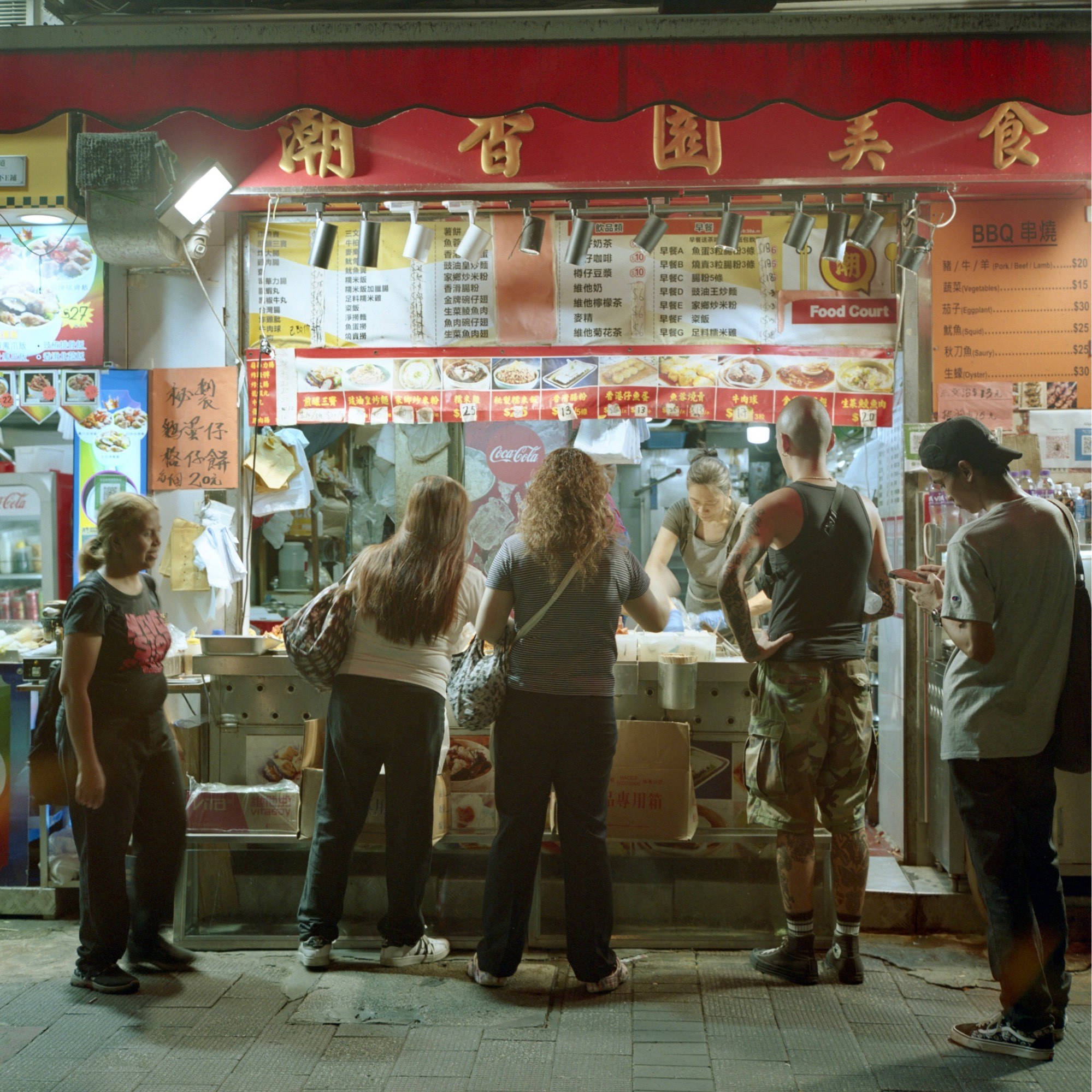 A colour film photo. Five people are in front of a street walk-up ordering their late night meals in Hong Kong, China. Monday, July 1, 2024.