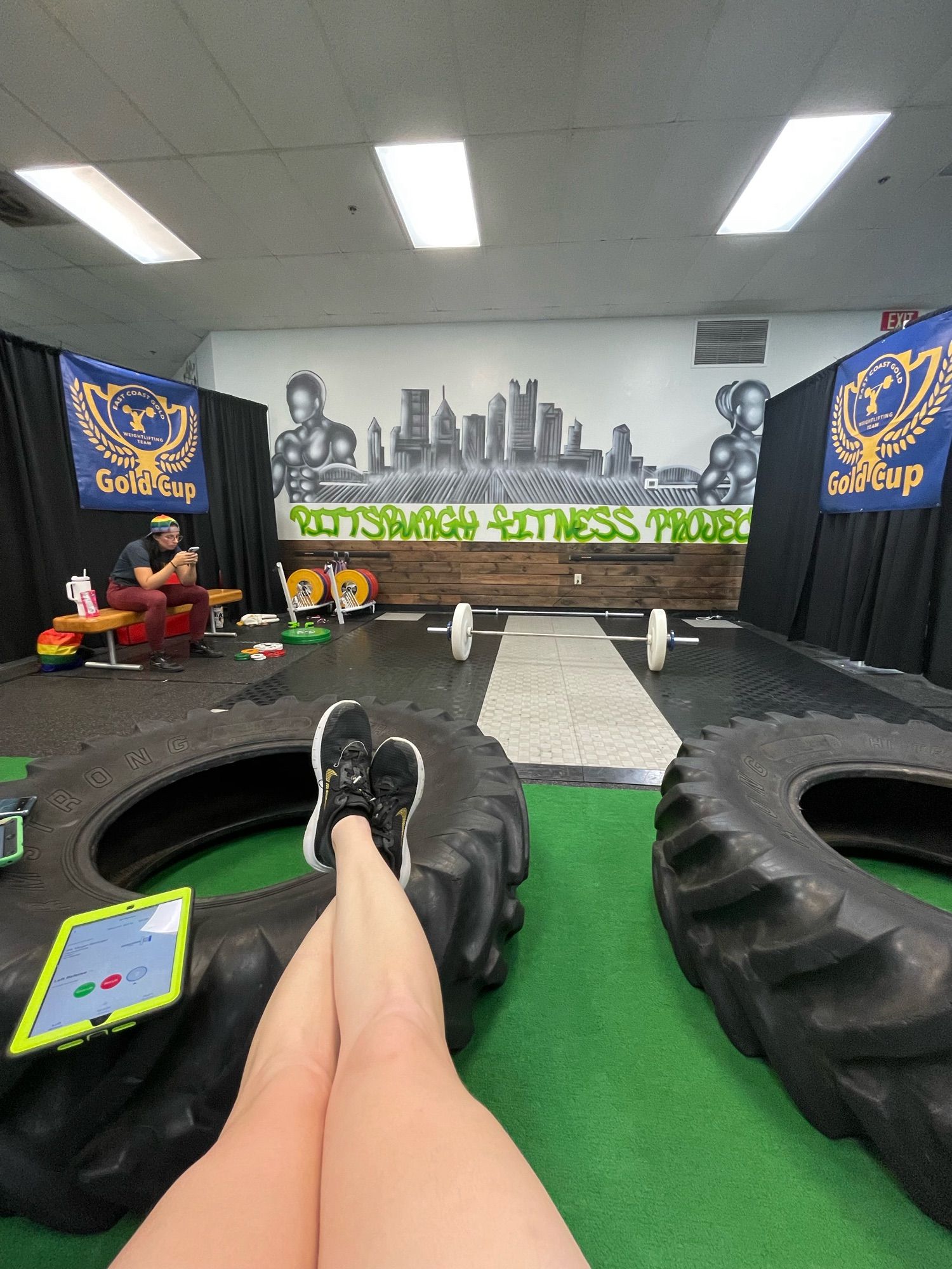 POV: you are a referee at a weightlifting meet that is about to start. A bar is loaded with about 25 kilos. Your legs are stretched out in front of you, and you’re using a tractor tire as a footrest.