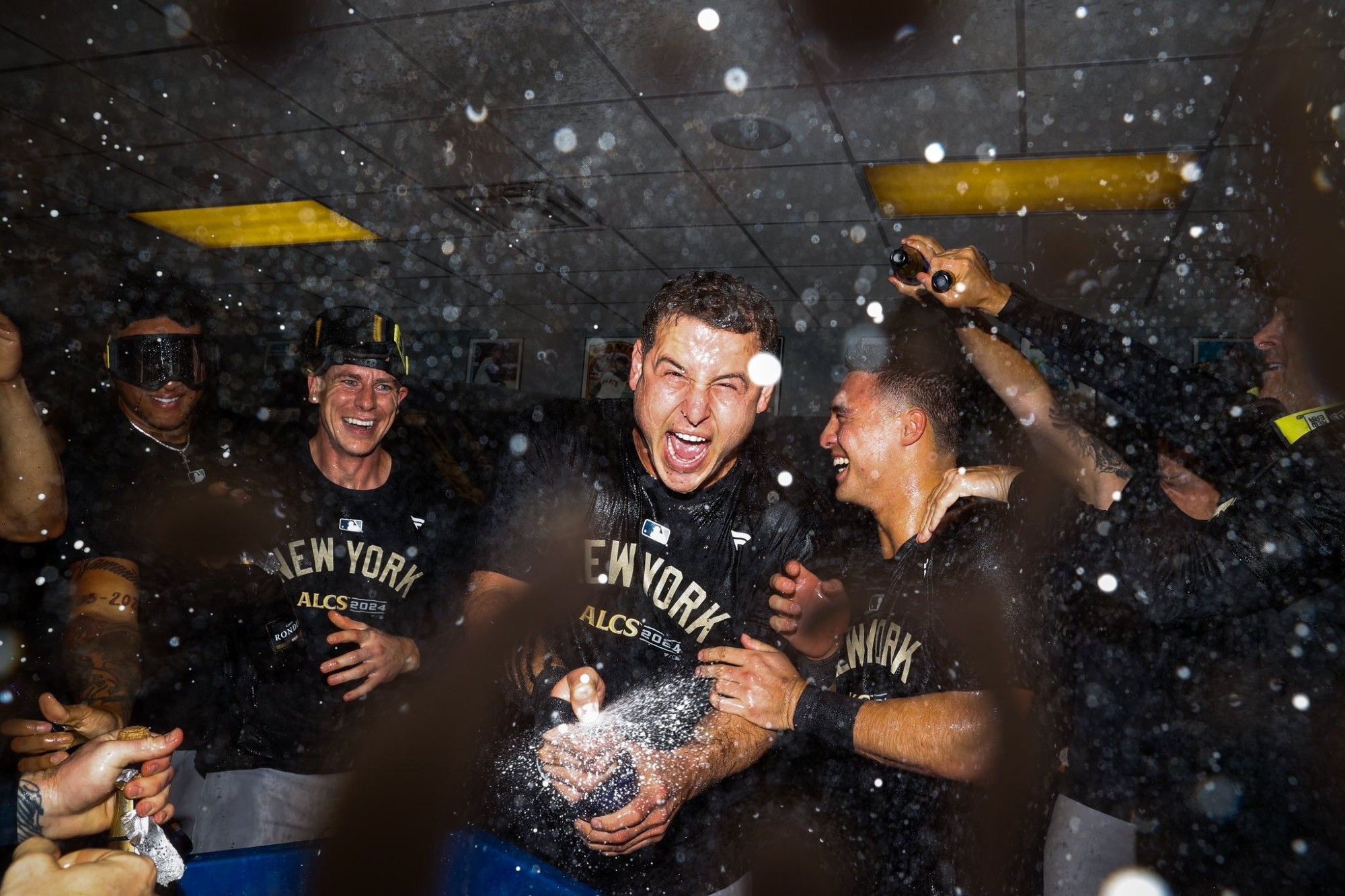 Anthony Rizzo spraying champagne directly at the camera while Ian Hamilton and Anthony Volpe look on.