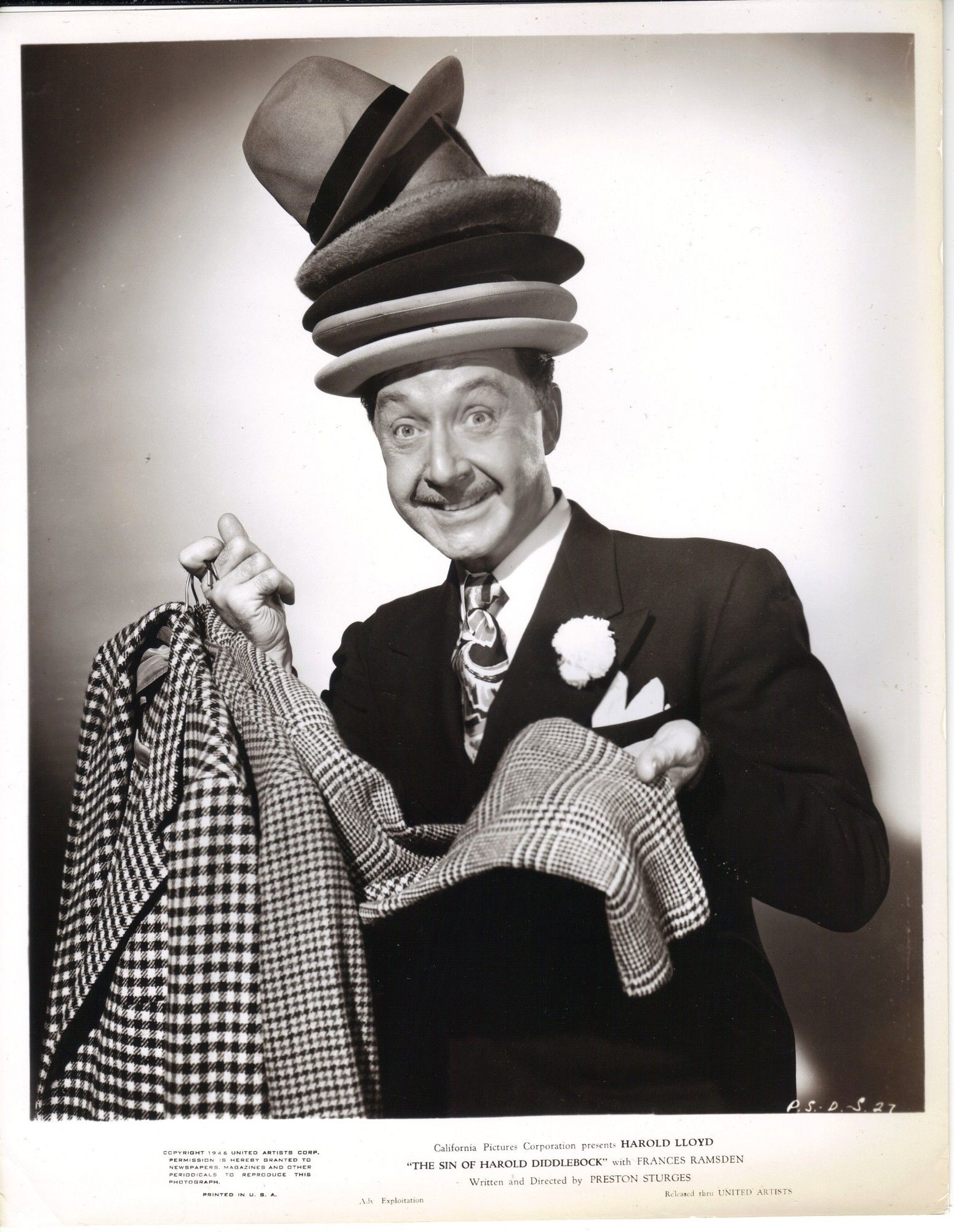 Franklin Pangborn smiles as he holds three suit jackets and wears five hats stacked on top of each other.