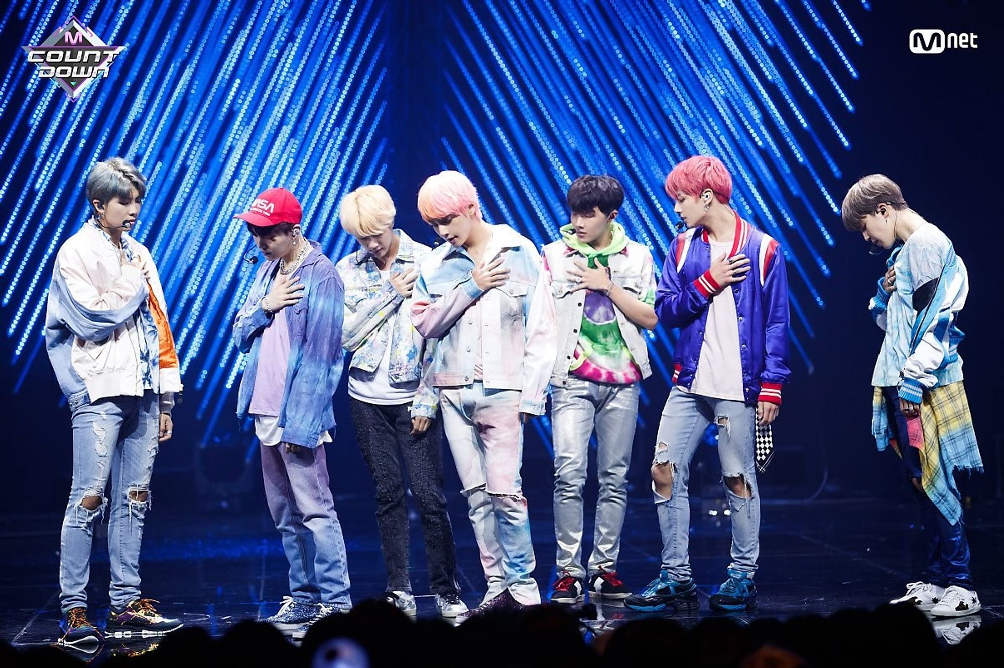 bts ot7 performing i'm fine on mcountdown in 2018. they're on stage in a lot of denim and casual jackets. jungkook is in his cherry hair era. they're standing contrapposto with one hand over their hearts, looking forlornly down and to the side.