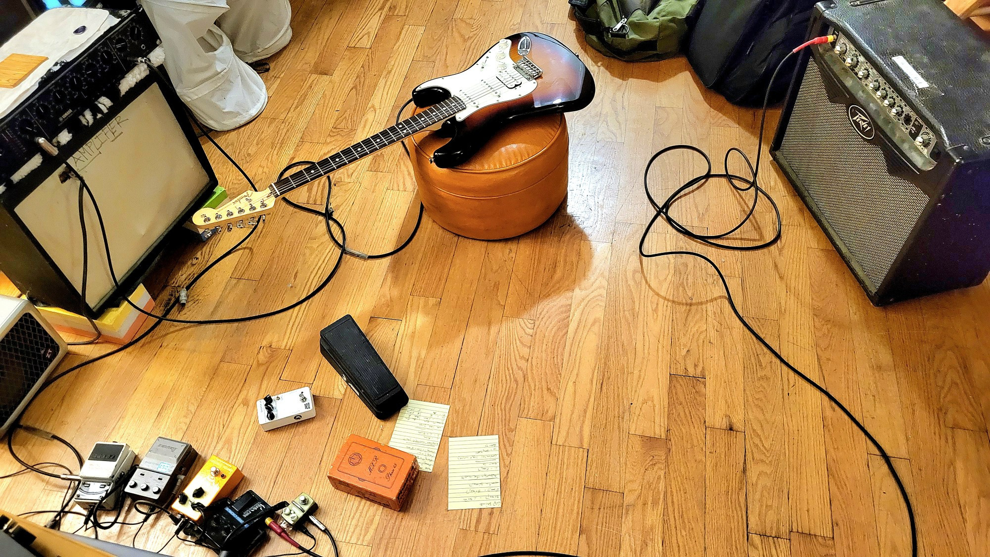 A fender Stratacaster on a footstool between two guitar amplifiers, a Peavey Vypyr and a ZT lunch box. The pedals are a Boss tuner, Ibanez DE7 delay, EarthQuaker Special Cranker, Vesta Fire Stereo Chorus which is splitting the signal, a Hotone Verb, a JHS 3 Series overdrive, a Cry Baby GCB-95 and a Bud Box MXR Phase 45, still in box. On the speaker cabinet to the left is a Yamaha E1010 rackmount modulating day.