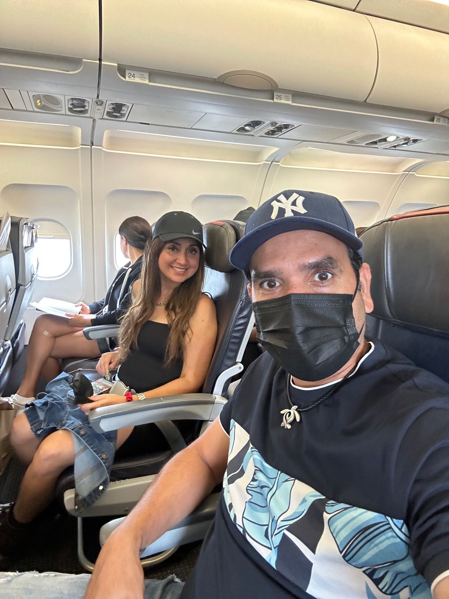 Picture selfie man with New York Yankees baseball hat, behind a woman next seat with Nike black hat 
