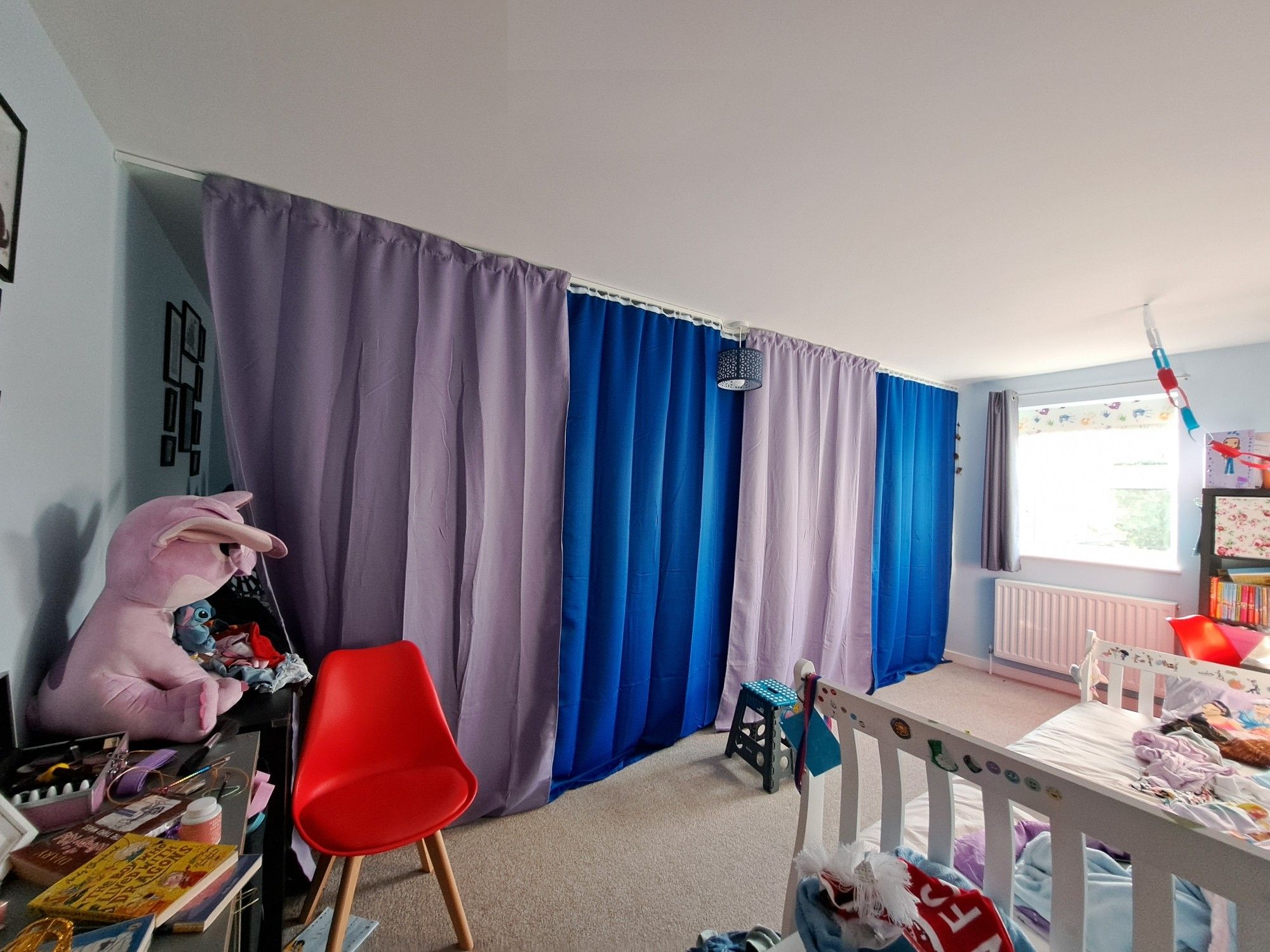 Image of a child's bedroom with purple and blue curtains dividing the room. The room is messy with all sorts of random toys and books