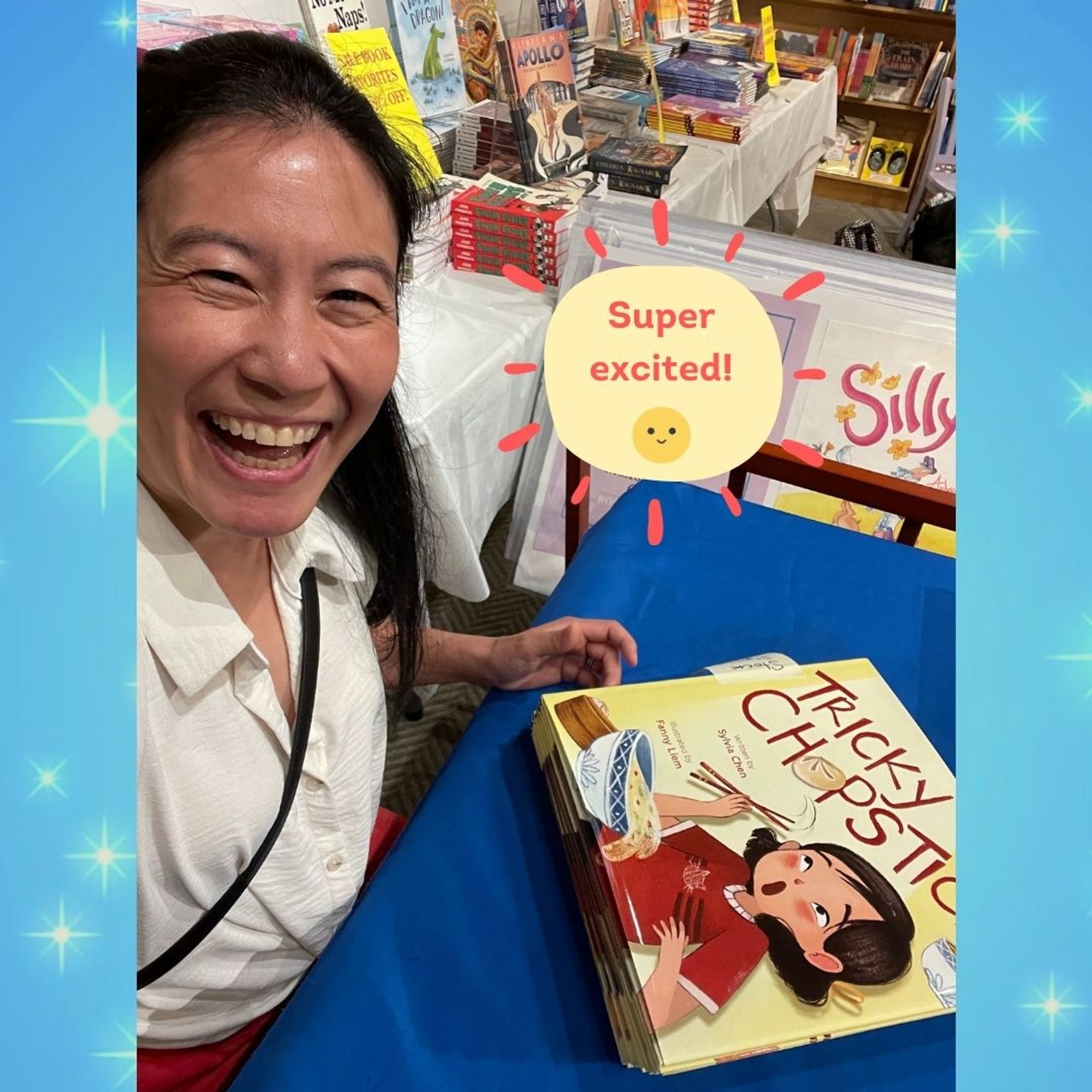 Selfie of author Sylvia Chen about to sign copies of TRICKY CHOPSTICKS on a blue tablecloth inside Books of Wonder in NYC.