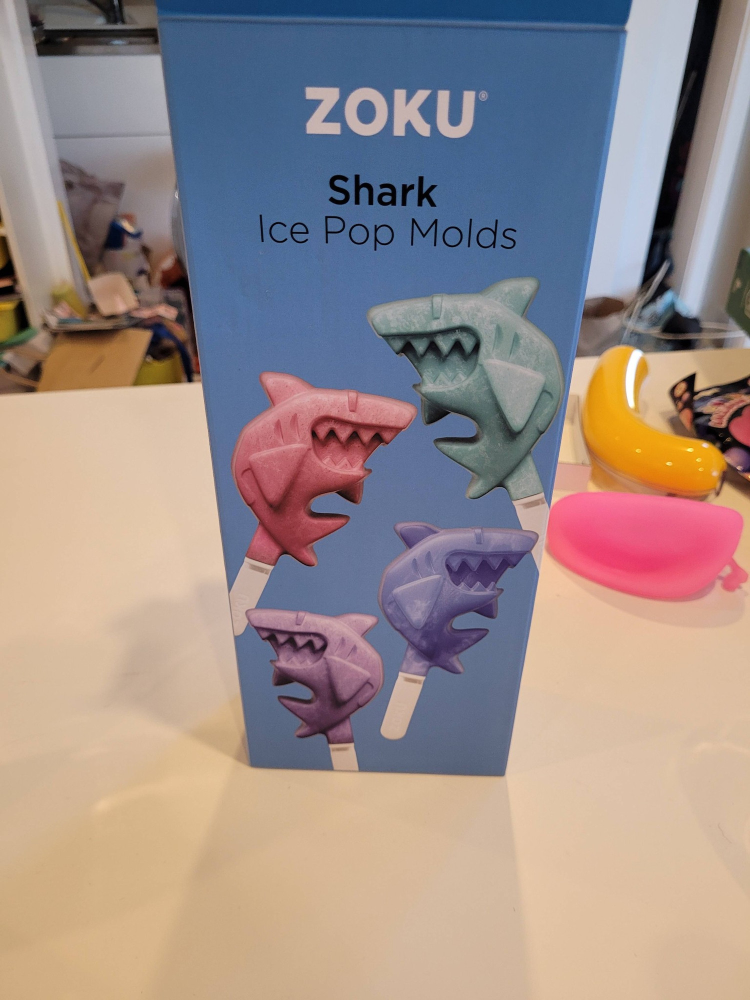 Ā box of zoku shark ice pop moulds on a white table.