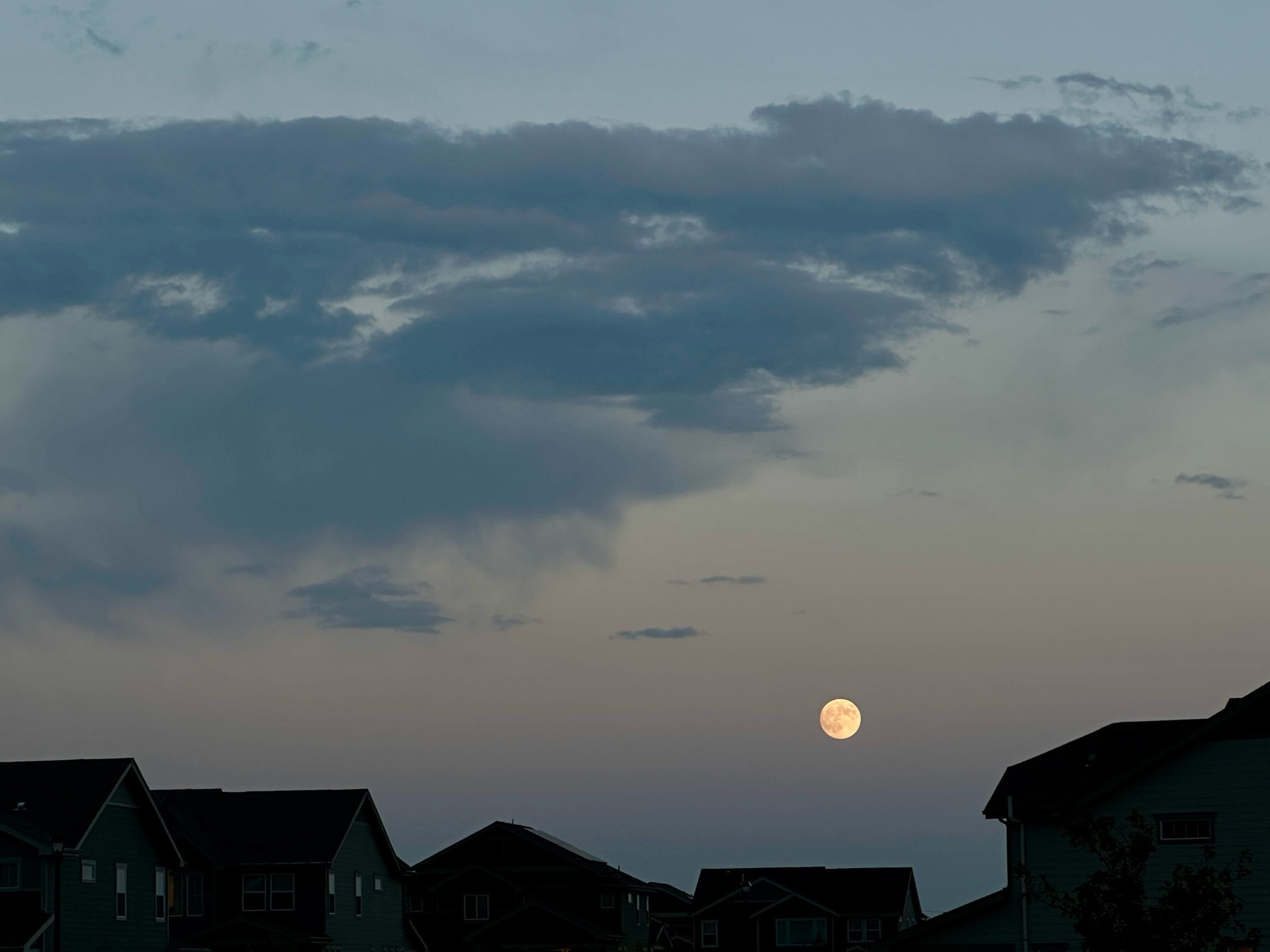 The moon and clouds over a dark silhouette of homes.