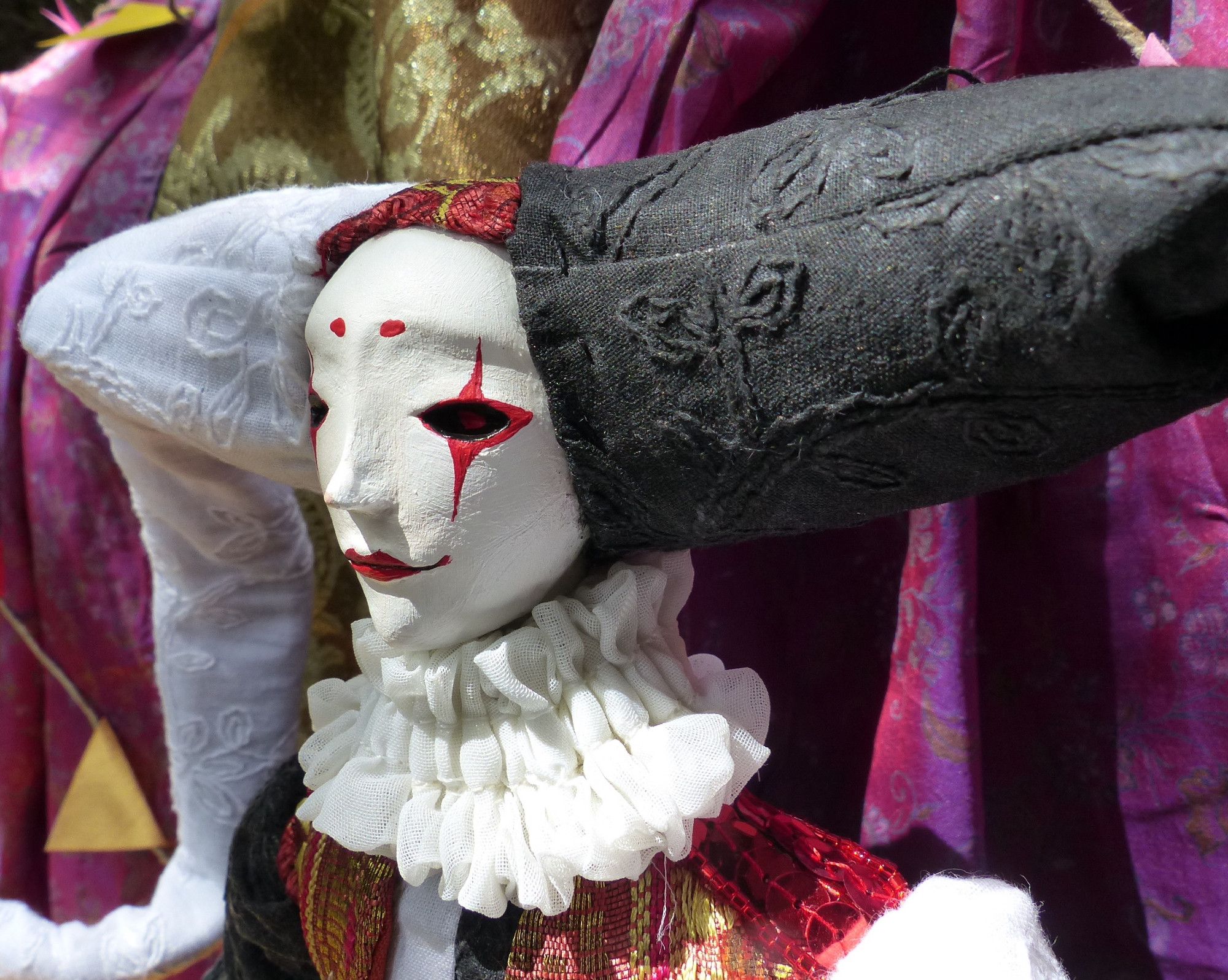 closeup picture of the face of a handcrafted posable soft jester doll with an asymetrical black and white diamond hat, white and red makeup