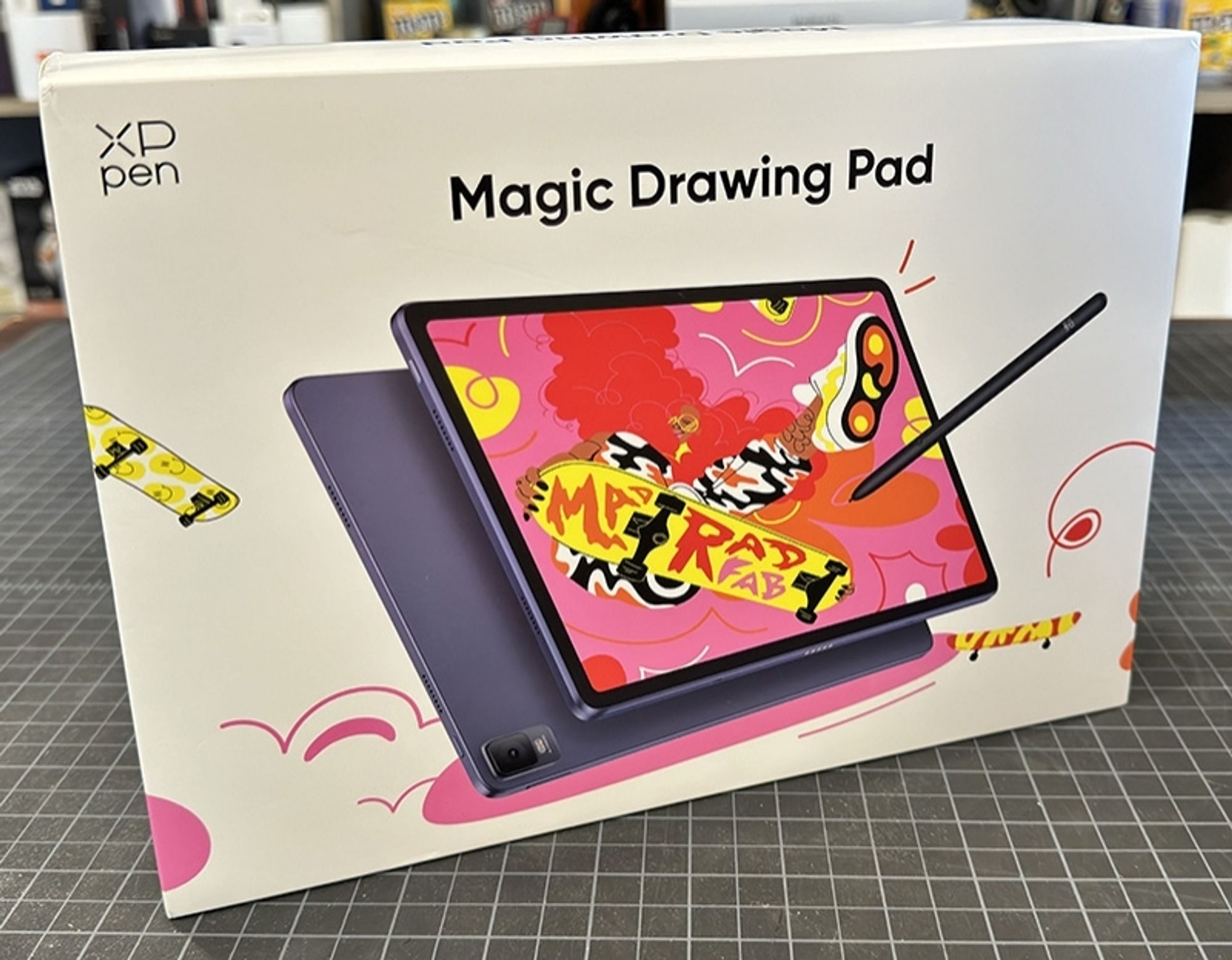 A photo of a tablet box on top of a self-healing cutting pad. The tablet is the XP-PEN Magic Drawing Pad, displaying an image of it in use of the box cover.