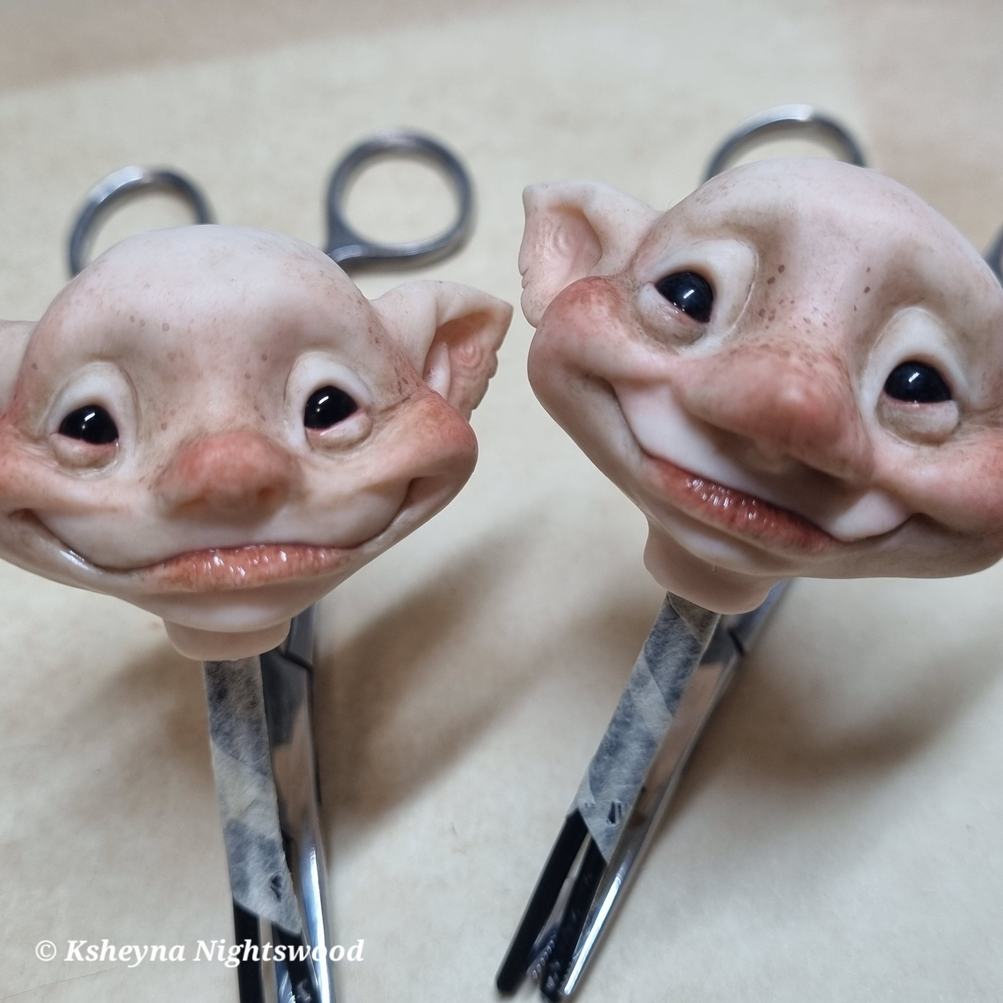 Two happy smiling faerie brownie heads, hand-sculpted from polymer clay and attached to wire.