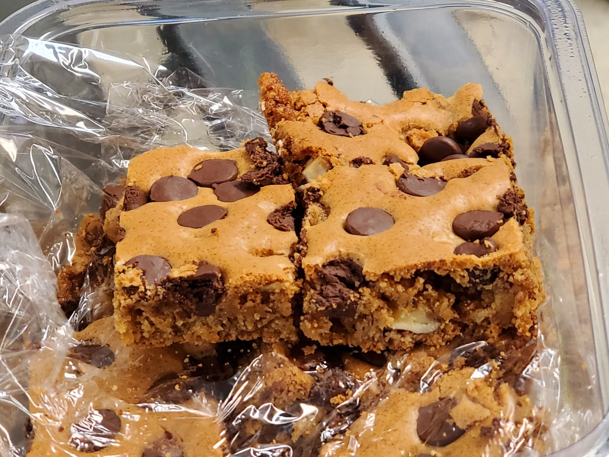 Scrumptious baked bars that are golden brown with chocolate chips and walnuts baked throughout. Nicely cut and stacked in cellophane in a clear tupperware.