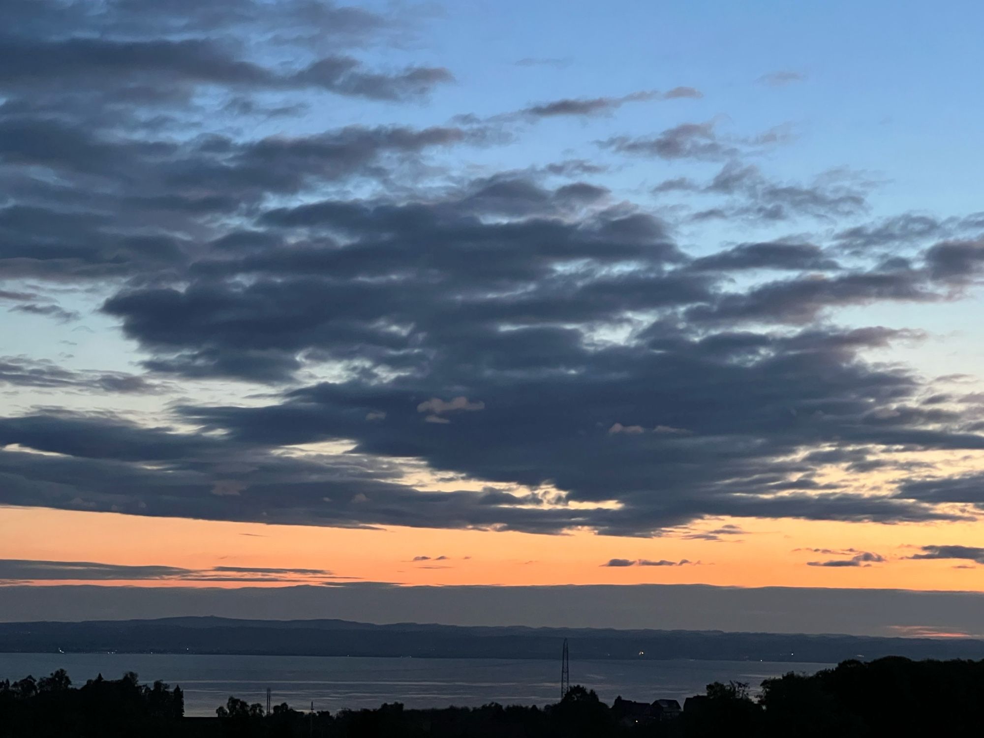 Morning sky before sunrise, over the bluegray horizon and lake are lighter bluegray clouds and a light orange sky