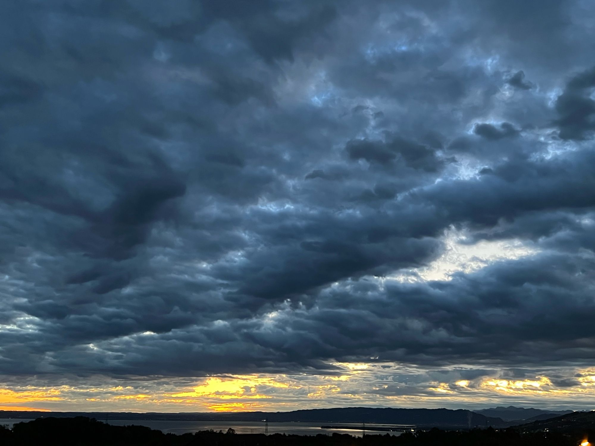 Dark grey clouds, a few over the horizon are sun litten yellow