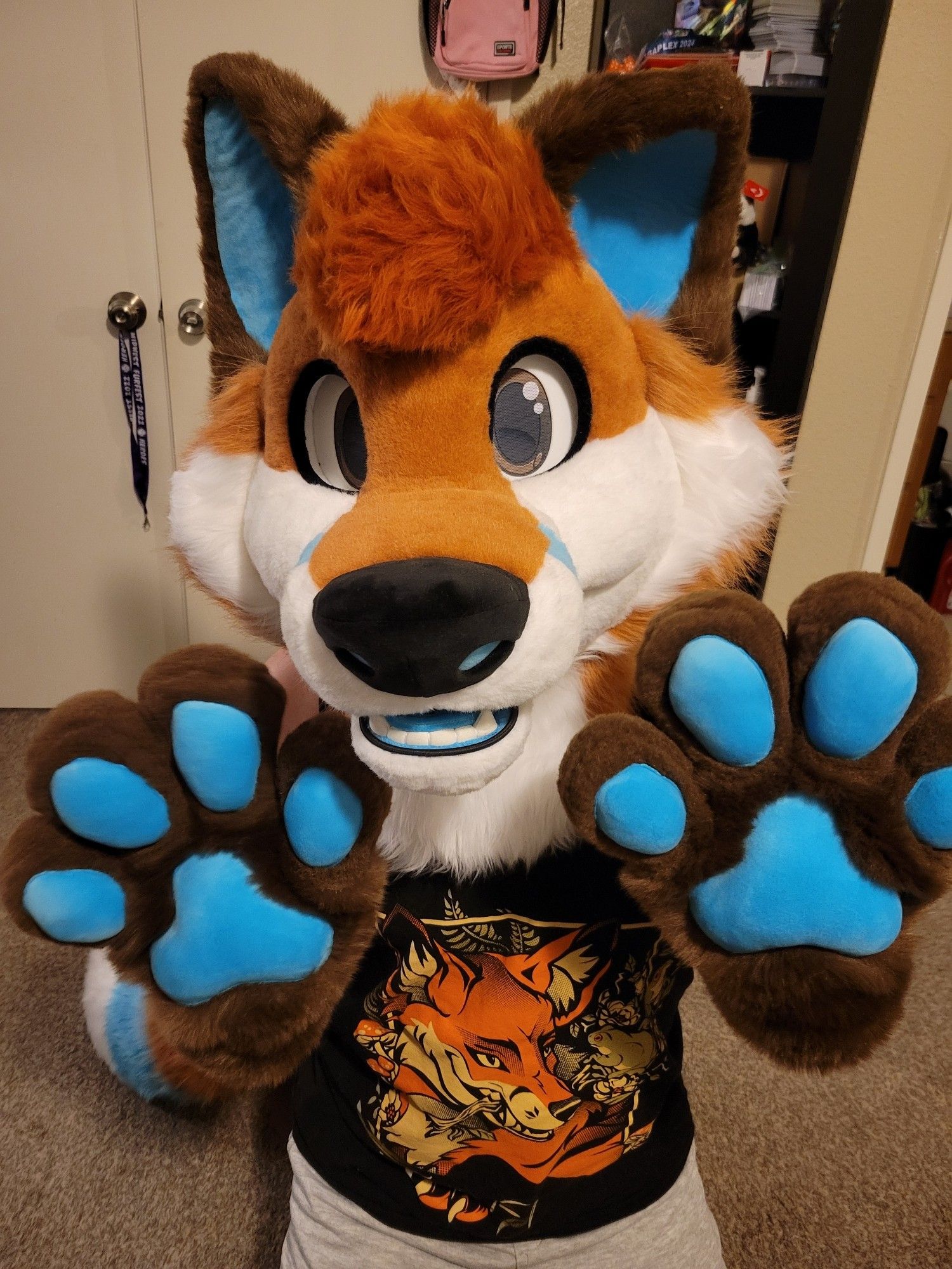 Fox fursuiter facing the camera with both paws up displaying paw pads