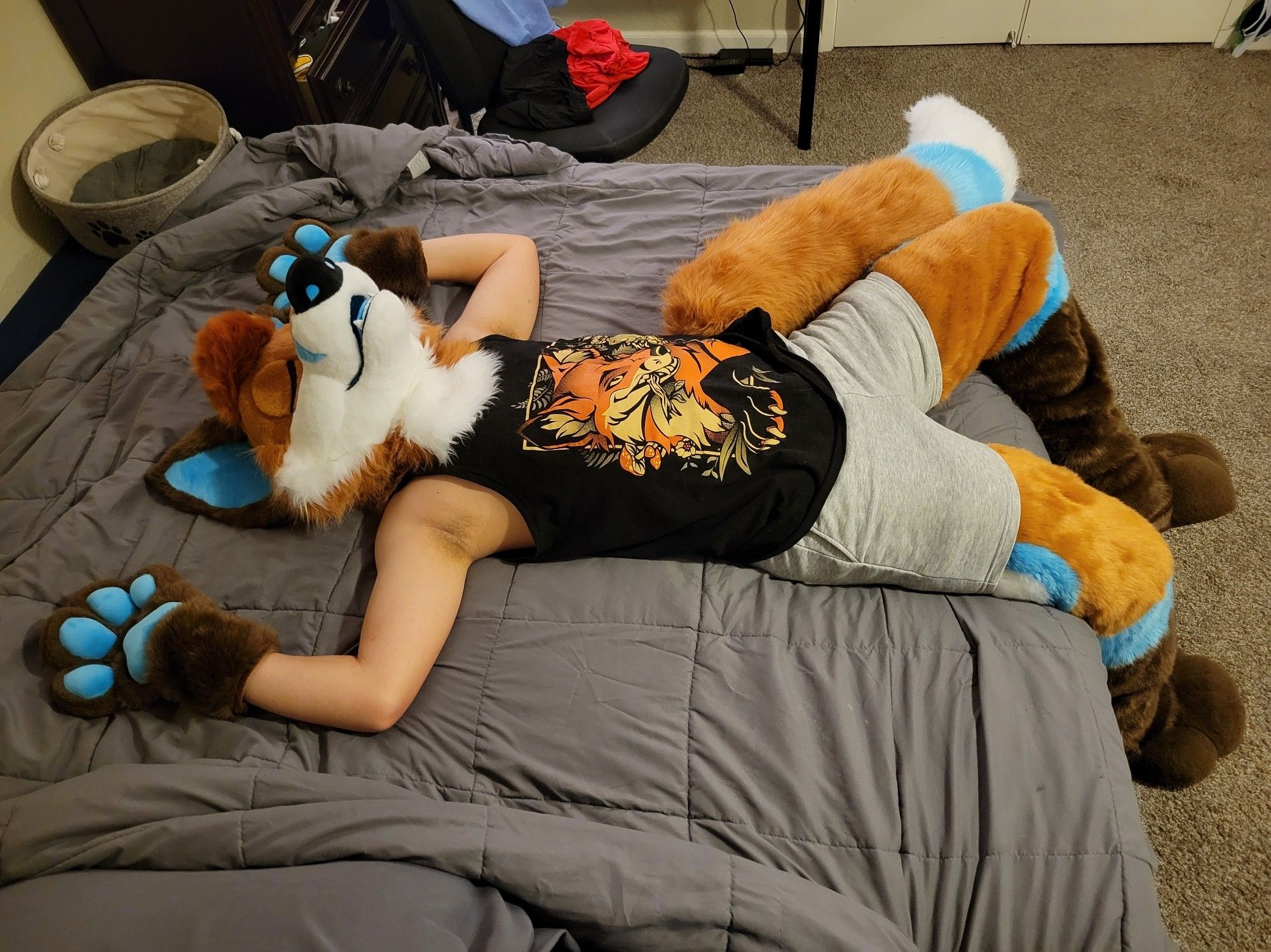 Fox fursuiter laying back on a bed with their eyes closed