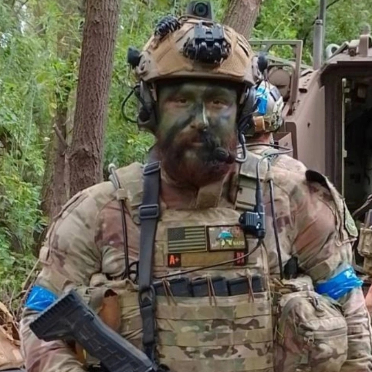 Trevor Reed in combat gear with weapon in Donbas, Ukraine standing behind an infantry fighting vehicle.