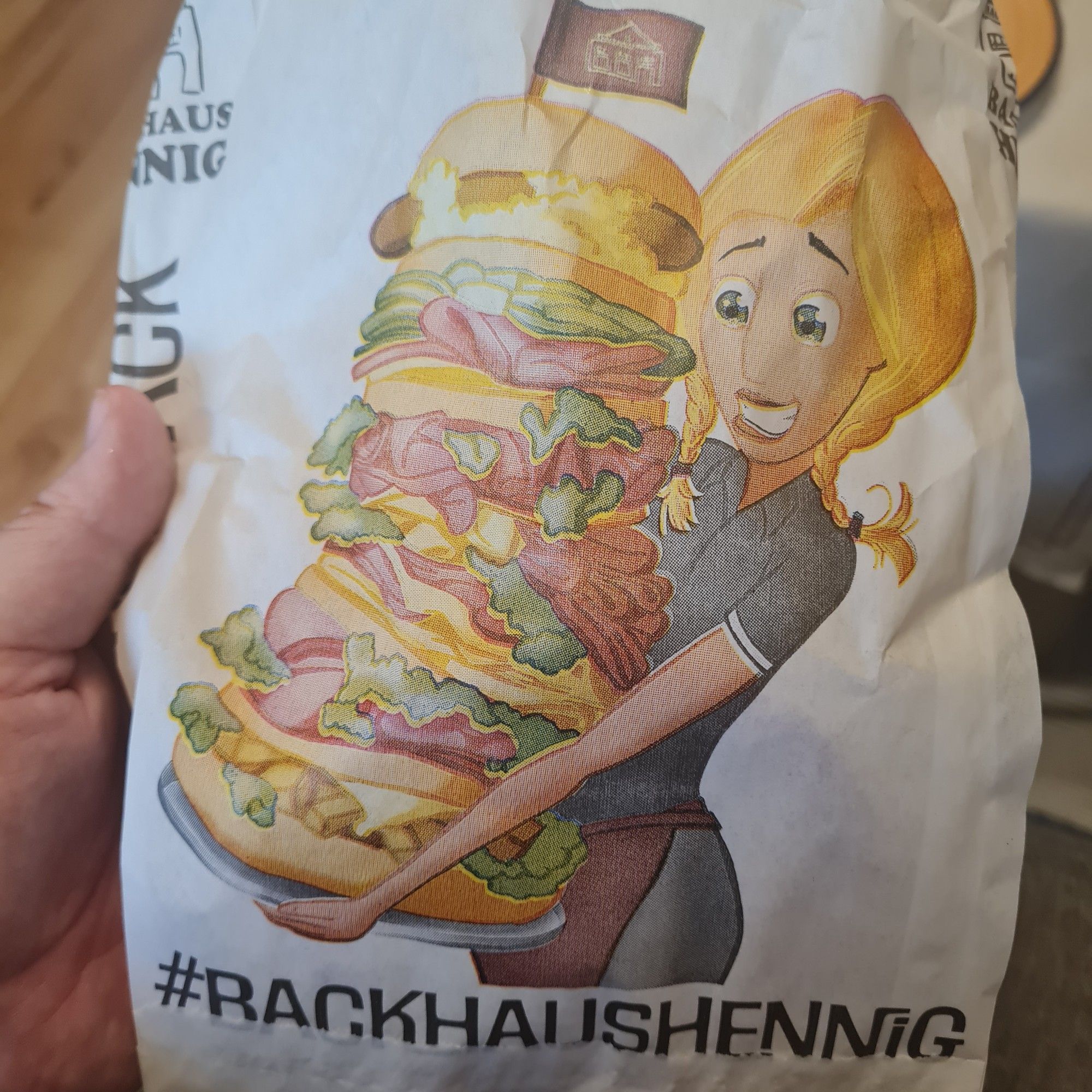 Brötchentüte vom Bäcker umme Ecke, eine Frau trägt ein riesiges Sandwich 