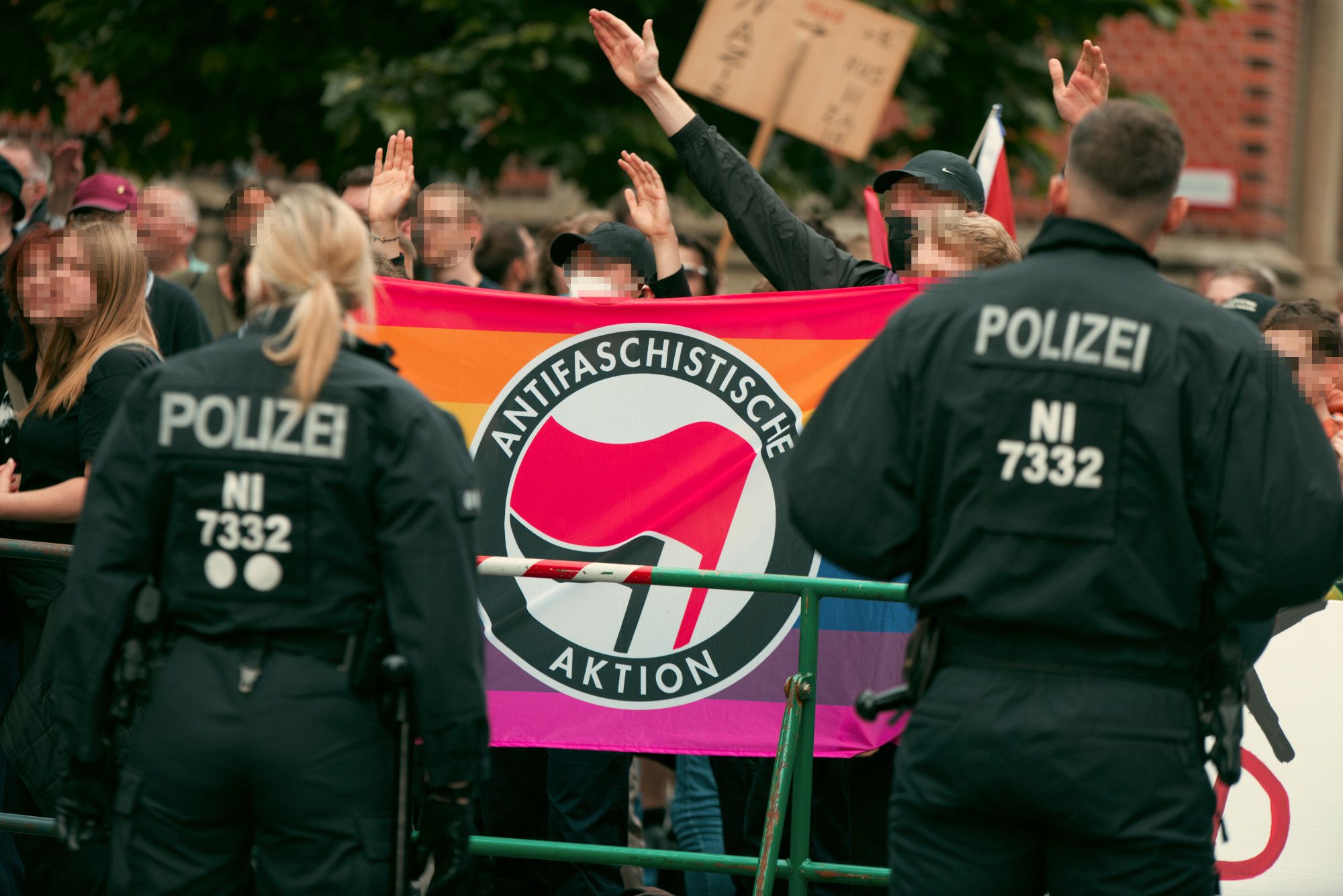 Eine Regenbogen-Antifa-Fahne im Gegenprotest hinter einer Polizeiabsperrung