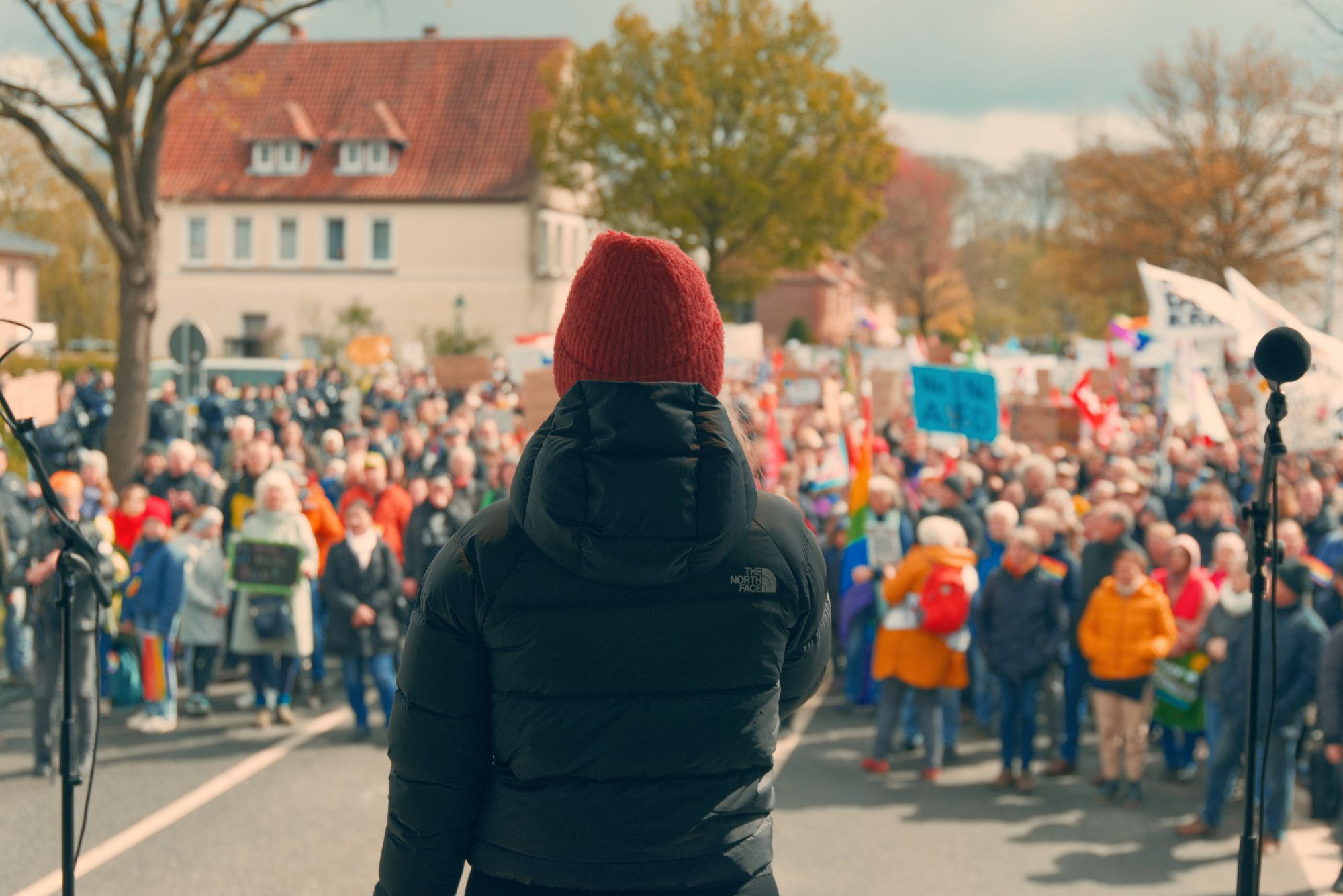 Eine Person spricht von der Bühne, im Hintergrund unscharf die Menschen auf der Kundgebung