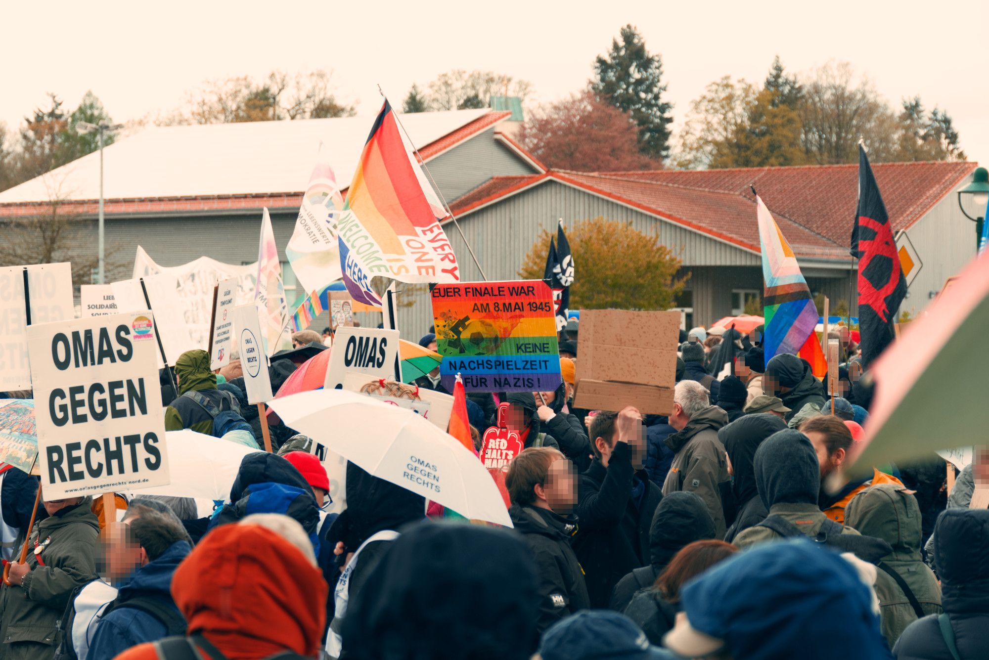 Bunte Fahnen und Schilder auf der Kundgebung. Im Hintergrund das Bürgerhaus