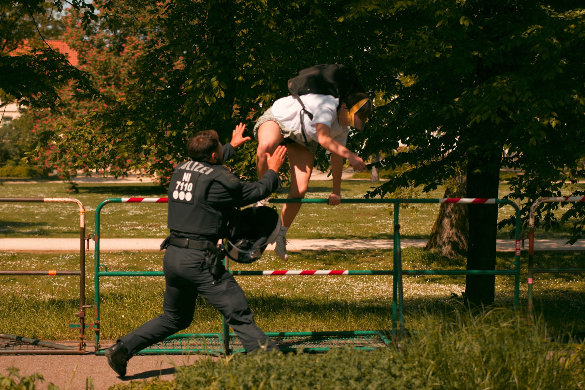 Am Rande der rechten Demoroute klettert eine Person über ein Hamburger Gitter. Gleichzeitig rennt ein Polizist mit erhobenen Armen auf die Person zu.