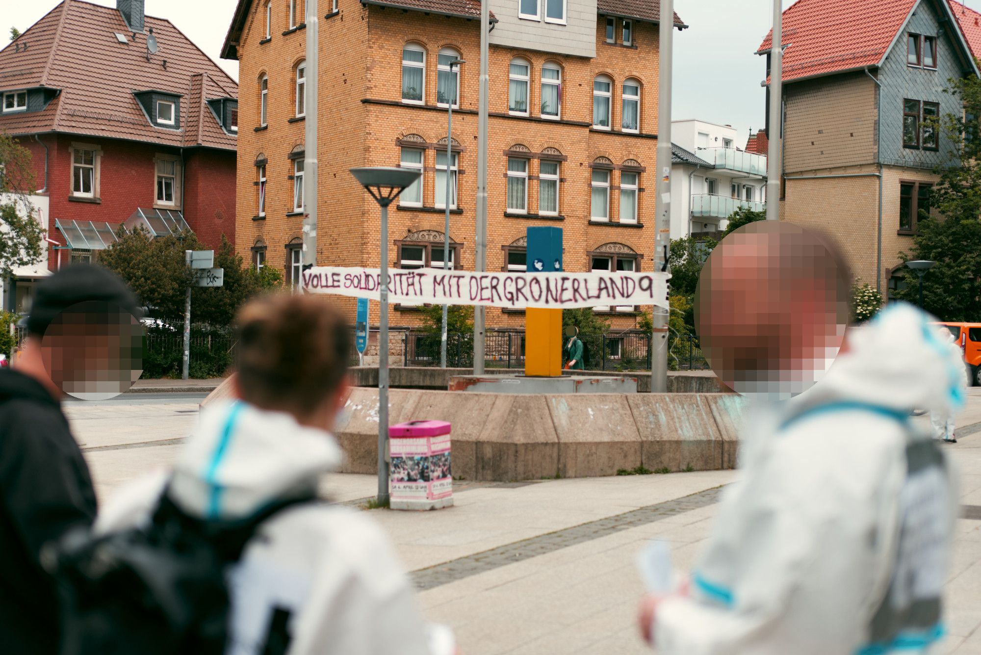 Einige Aktivist*innen der Aktion, im Hintergrund ein weißes "Volle Solidarität mit der Gronerland 9" Transparent, das zwischen zwei Fahnenstangen gespannt ist