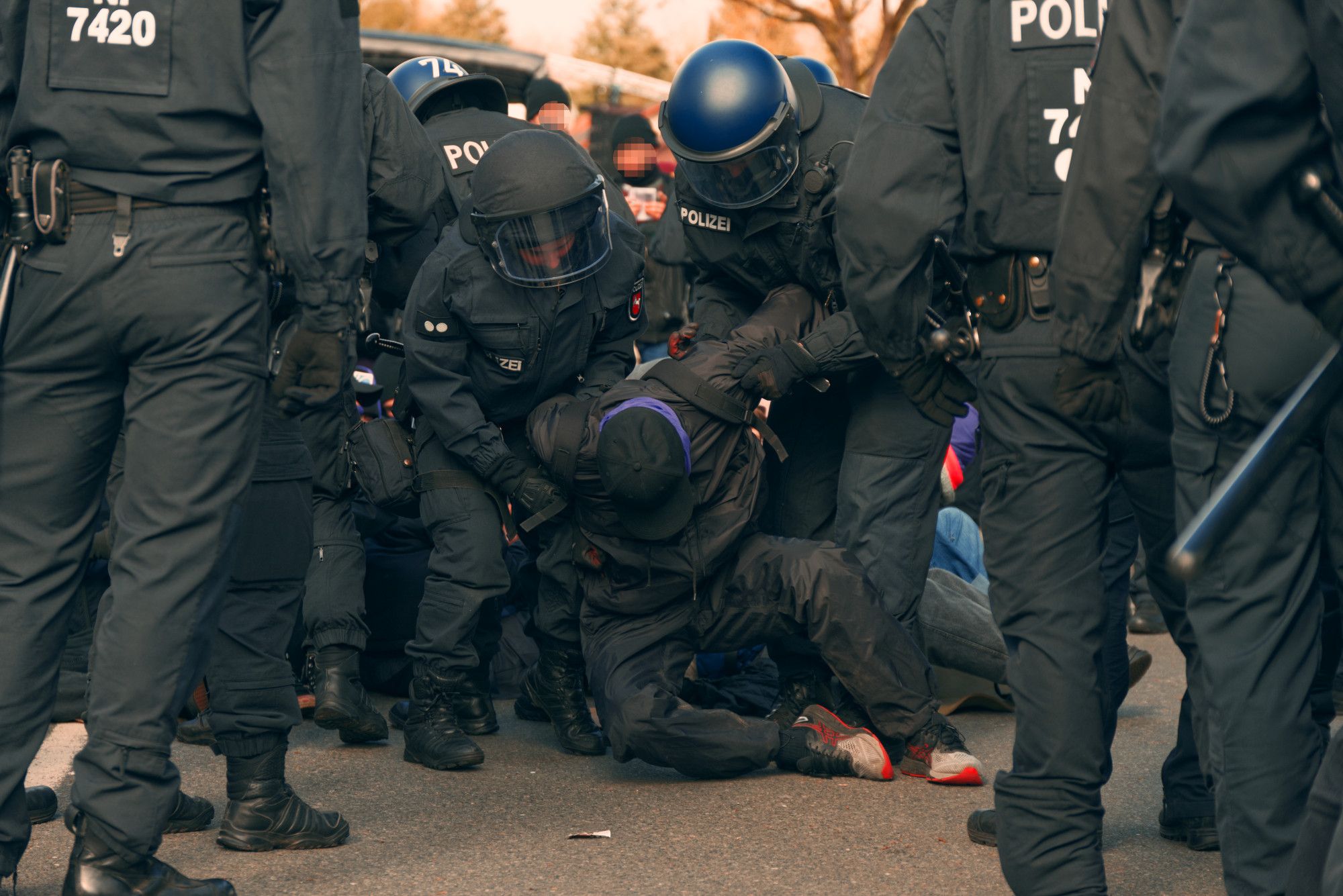 Räumung einer Blockade durch die Polizei. Zwei Beamt*innen packen dabei eine Person aus der Blockade an den Schultern