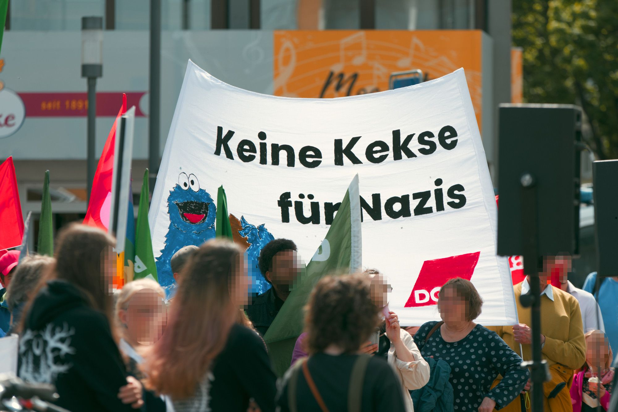 Blick über einen Teil der Auftaktkundgebung mit einem weißen "Keine Kekse für Nazis" Transparent des DGB mit einem Bild des Krümelmonsters daneben.