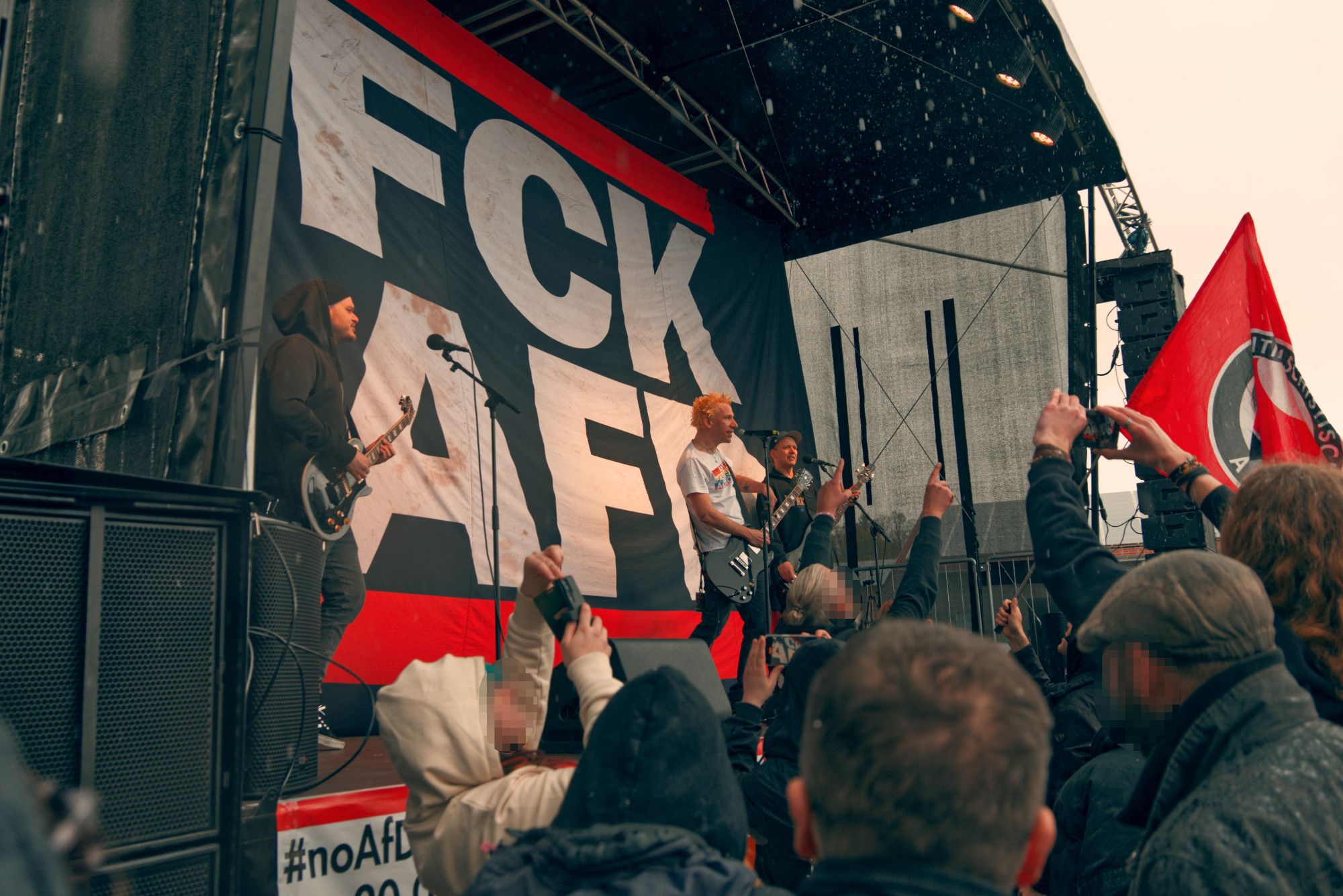 Die Band ZSK vor einem großen FCK AFD Banner auf der Bühne. Davor Menschen, die zur Musik tanzen.