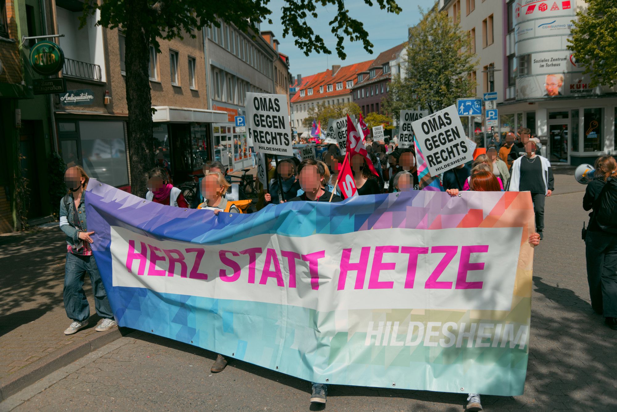 Buntes "Herz statt Hetze Hildesheim" Fronttransprent der Demonstration. Dahinter viele Menschen, einige mit weißen "Omas gegen Rechts" Schildern