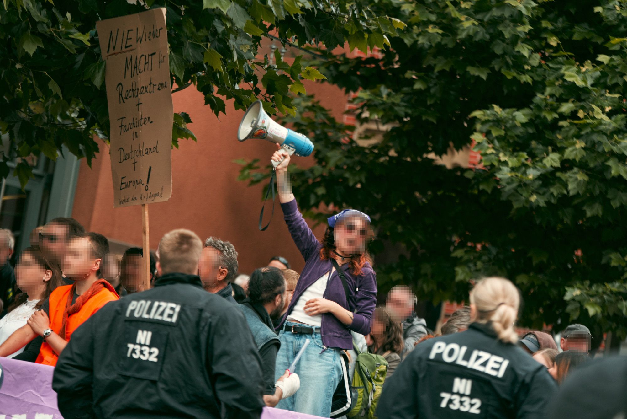 Eine Person aus dem Gegenprotest, die eine hand mit Megafon emporstreckt