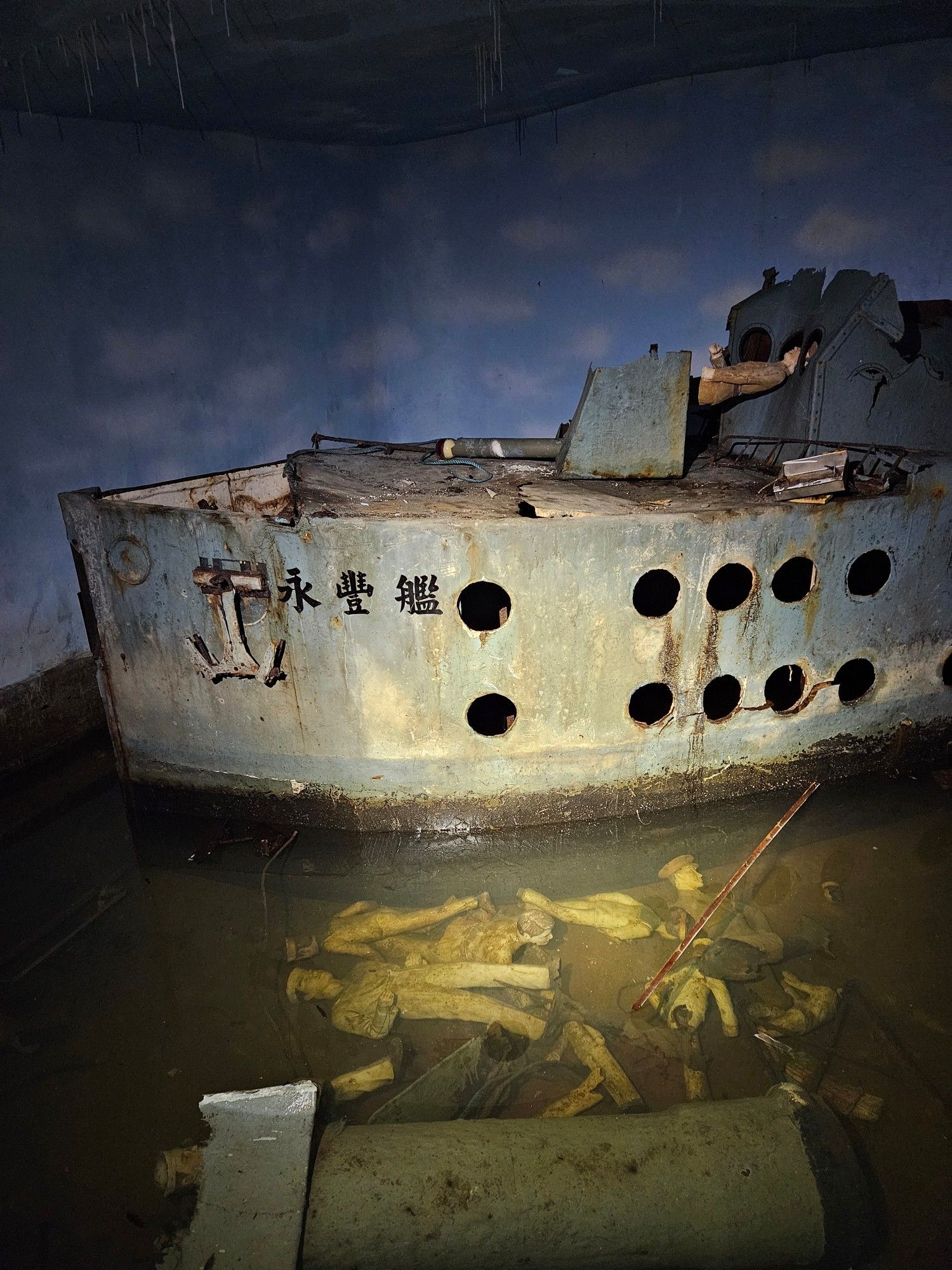 A scene inside a former attraction in a tunnel, this one depicting a warship named Yong Feng. What looks to be crew members can be discerned in the murky brown water flooding the bottom of the diorama.