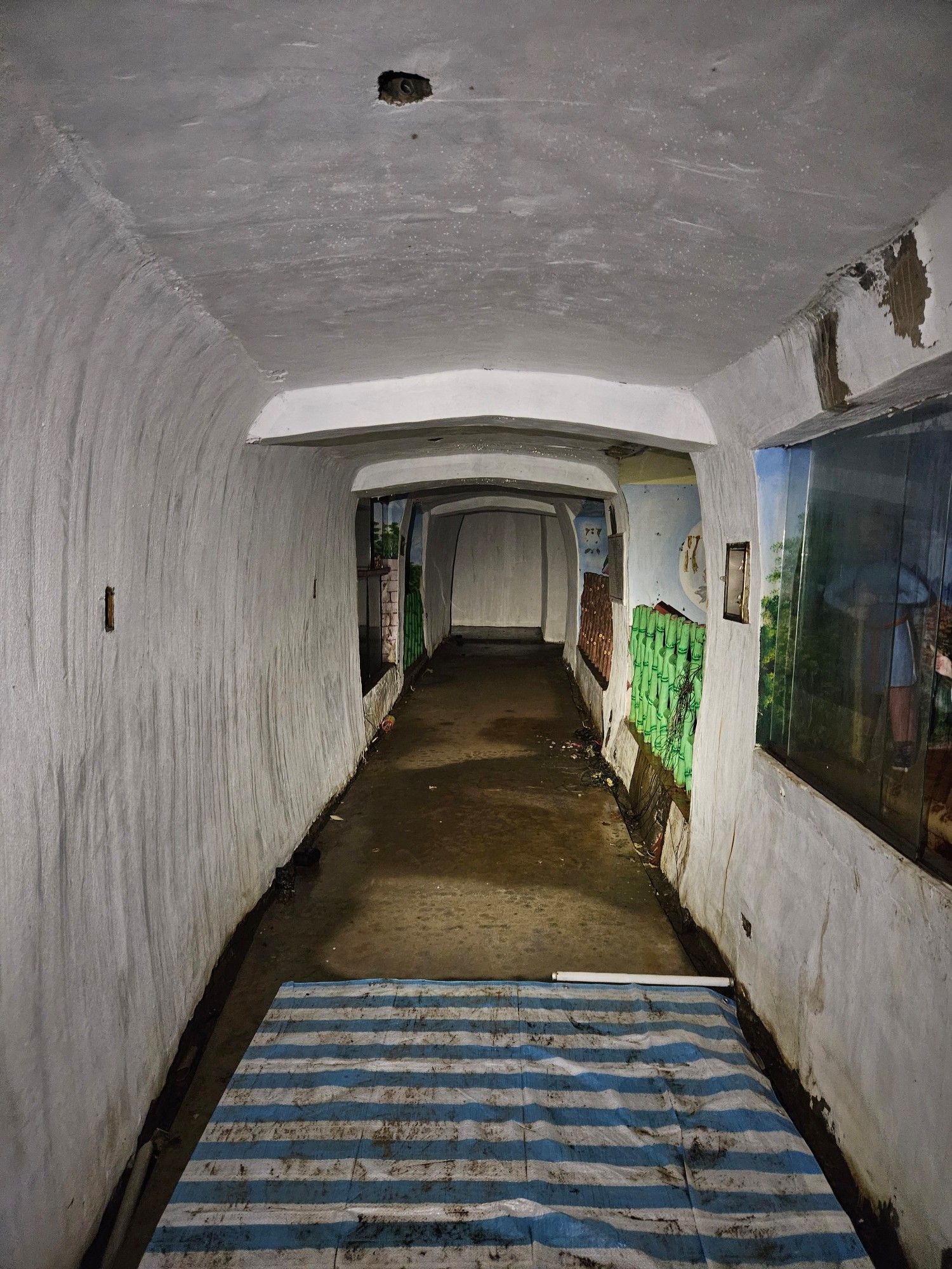 An abandoned tunnel, painted white, with some alcoves on the right concealing dioramas from Chinese mythology.