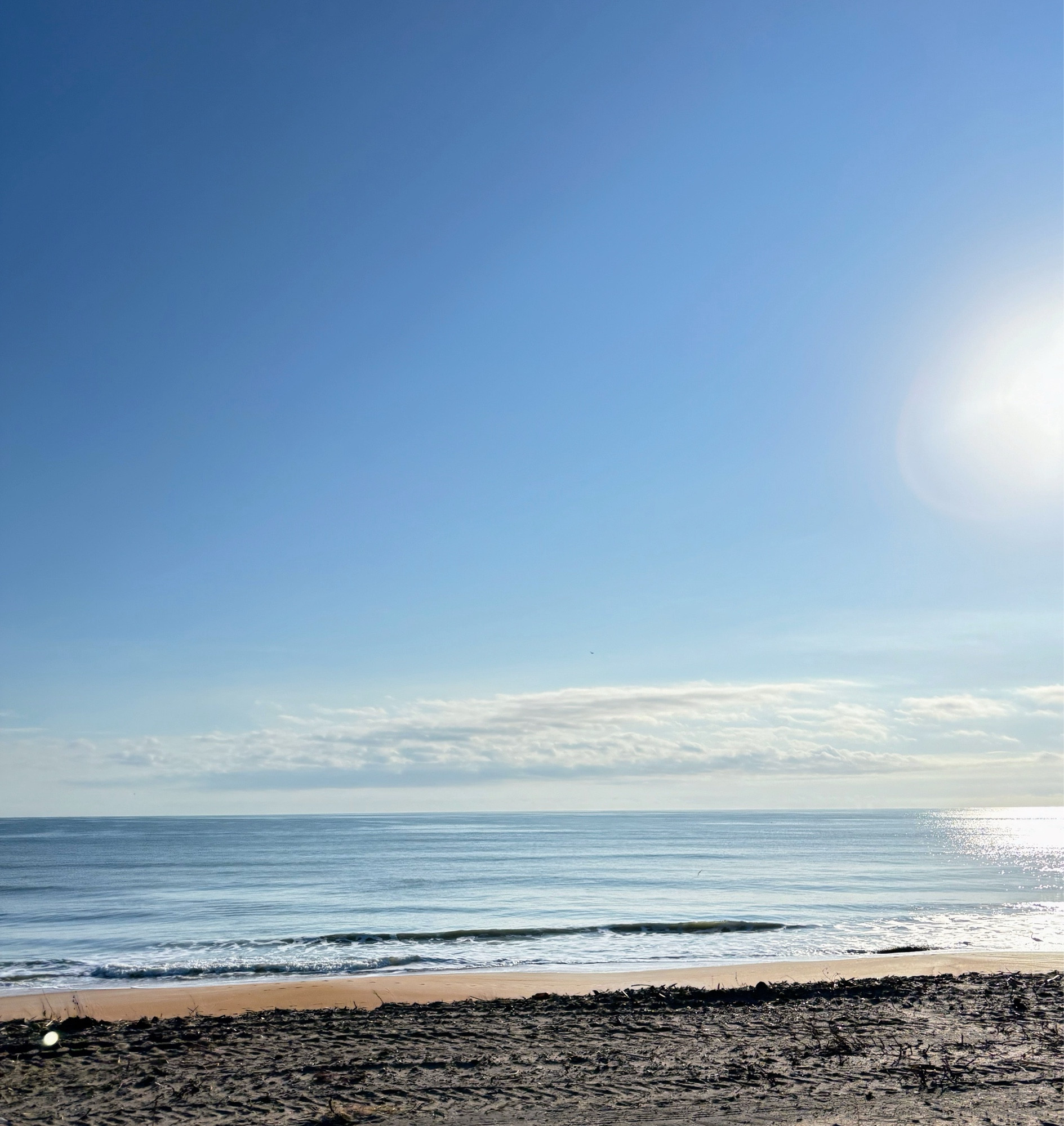 Ocean with sun shining and reflecting. Orange sand and white sand with vehicle tracks to pack the new sand in.