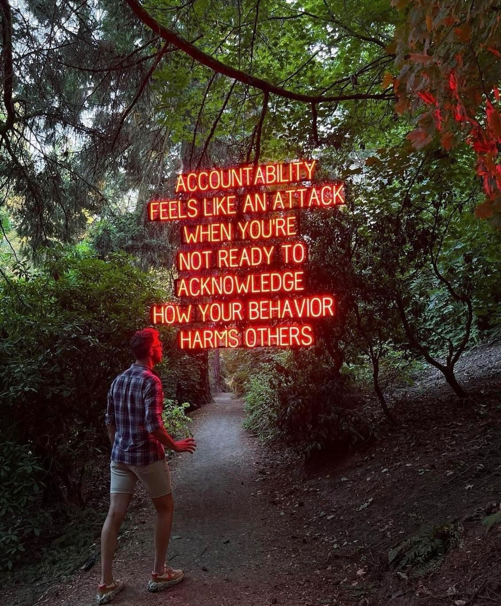 The whitest guy ever on a hole in some park who stumbles across hovering neon letters glowing in the evening, splashing red on him like a warning: Accountability looks like an attack when you're not ready to acknowledge how your behavior harms others