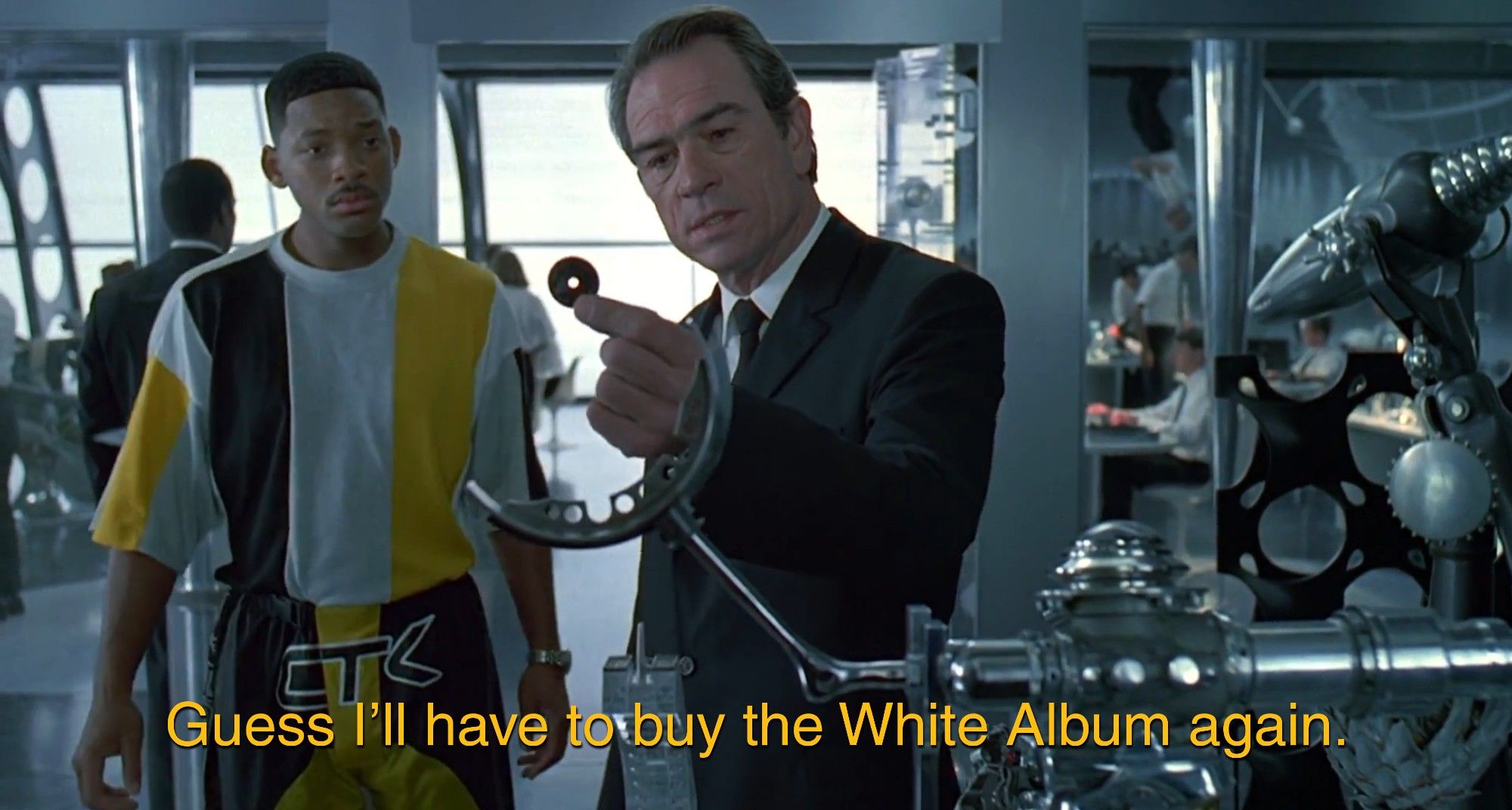 Tommy Lee Jones as Agent K in Men in Black stands in a 90s suit, with Will Smith as soon to be Agent J standing a bit behind him in a black white and yellow 90s outfit. Agent K is holding a very tiny tiny CD and is saying "Guess I'll have to buy the White Album again."