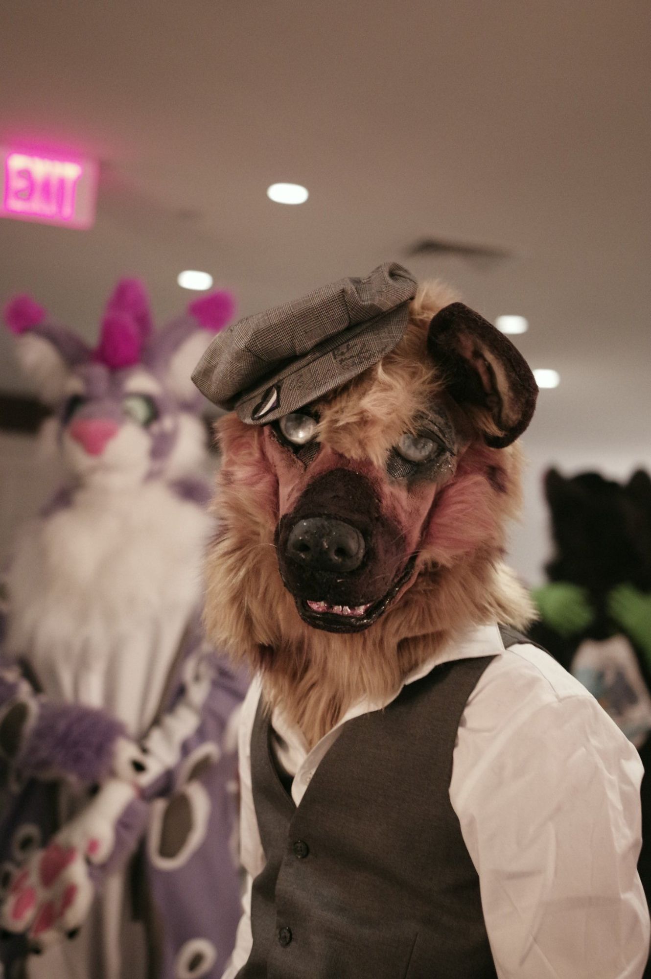 a photo by tom of ME! in my hyena fursuit partial. i'm wearing a dress shirt and vest, with a newsie cap over one ear (it has a little heart with asexual pride colors on it)  the head was made by me on a crystumes costume base, and has a sort of blend of realism and muppet action to it. Drifa the snynx (snow leopard/lynx) is visible but out of focus behind me. My suit/hyena sona goes by the name Cial (pronounced like "kyle")