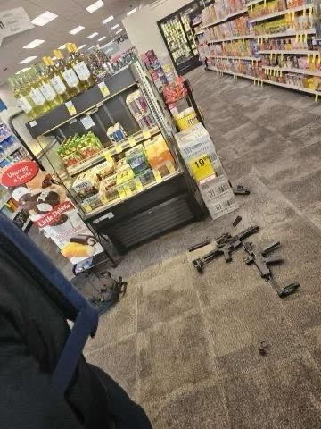 Two automatic rifles, some rifle magazines, and a backpack on the floor of a CVS