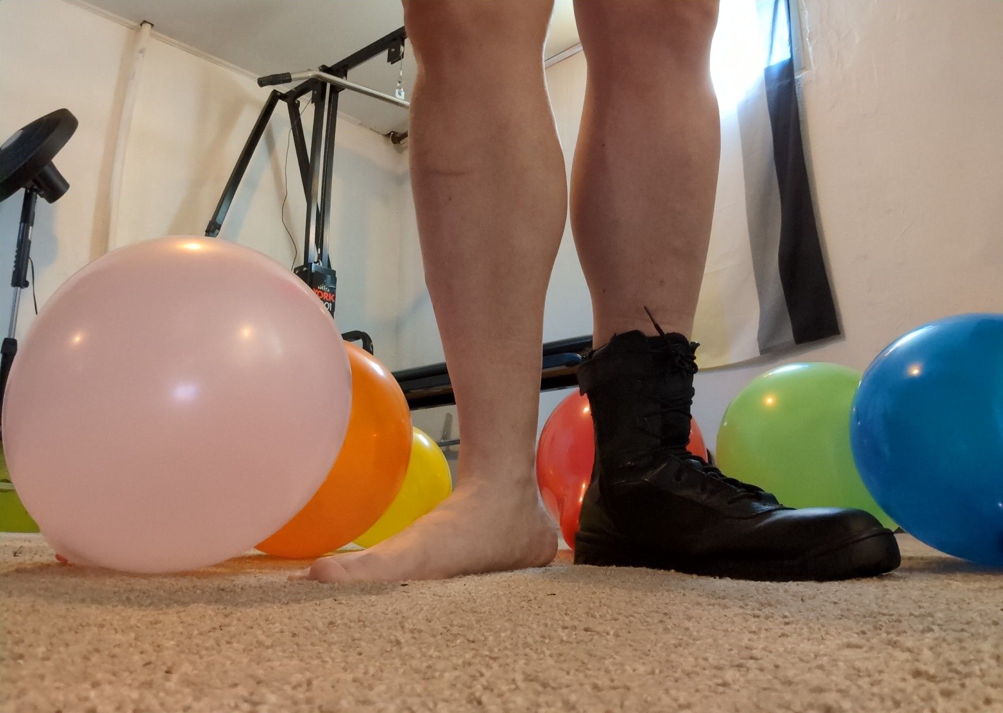 A guy with one foot bear in the other wearing a leather boot standing in a pile of balloons