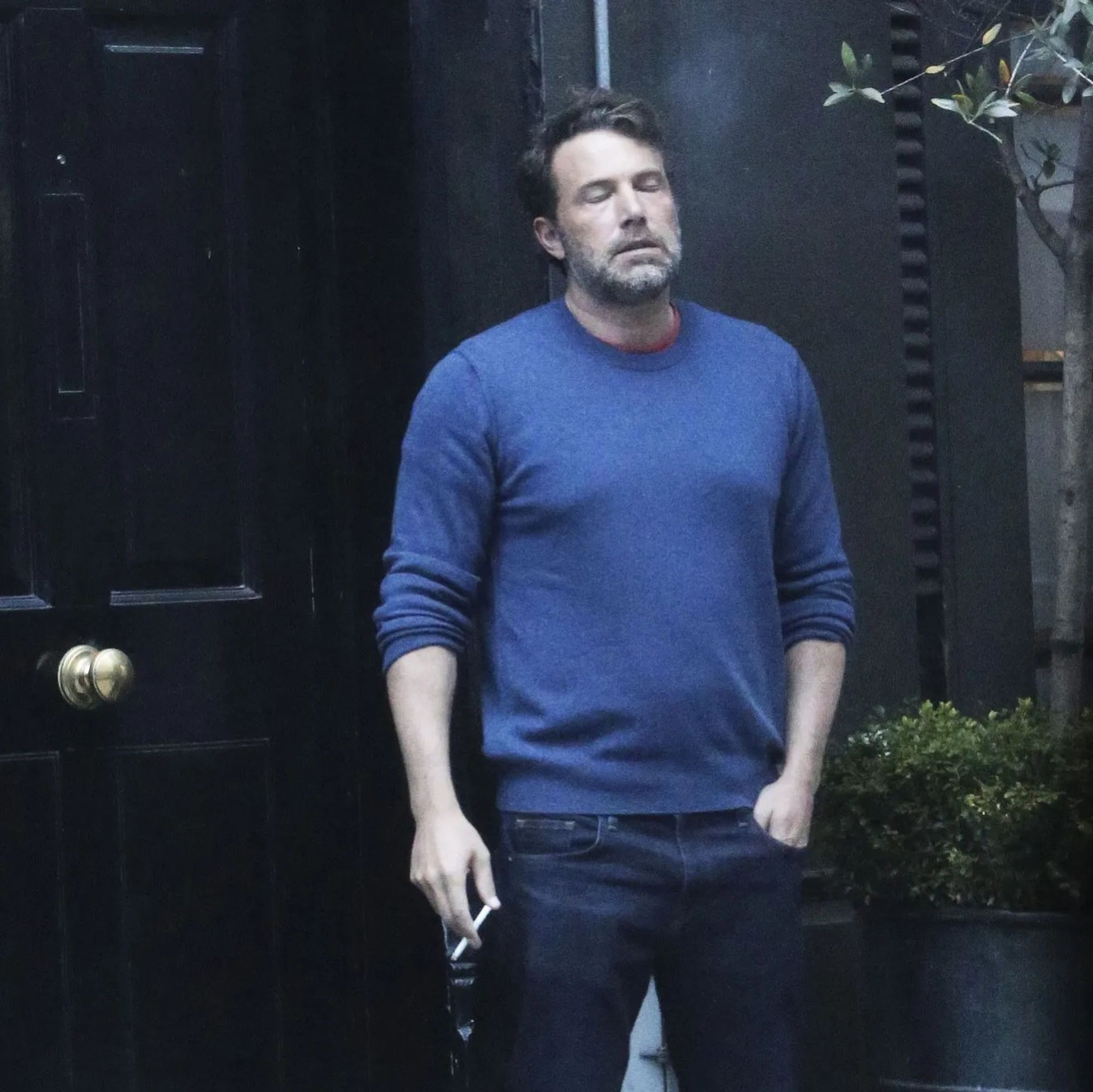 Ben Affleck smoking in front of a door, looking like life fucked him hard.