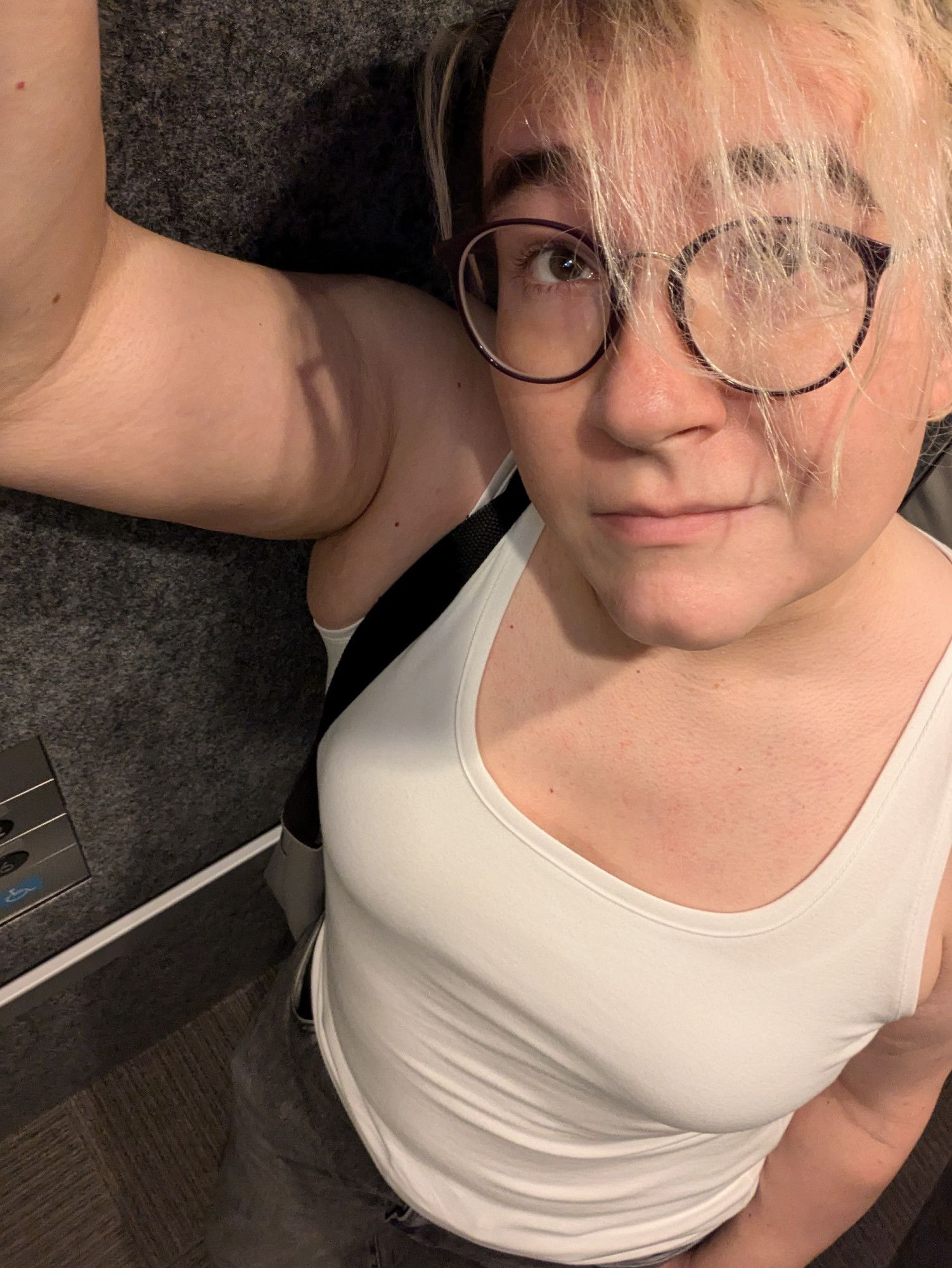 trans girl with big round glasses in a low-cut tank top and grey jeans