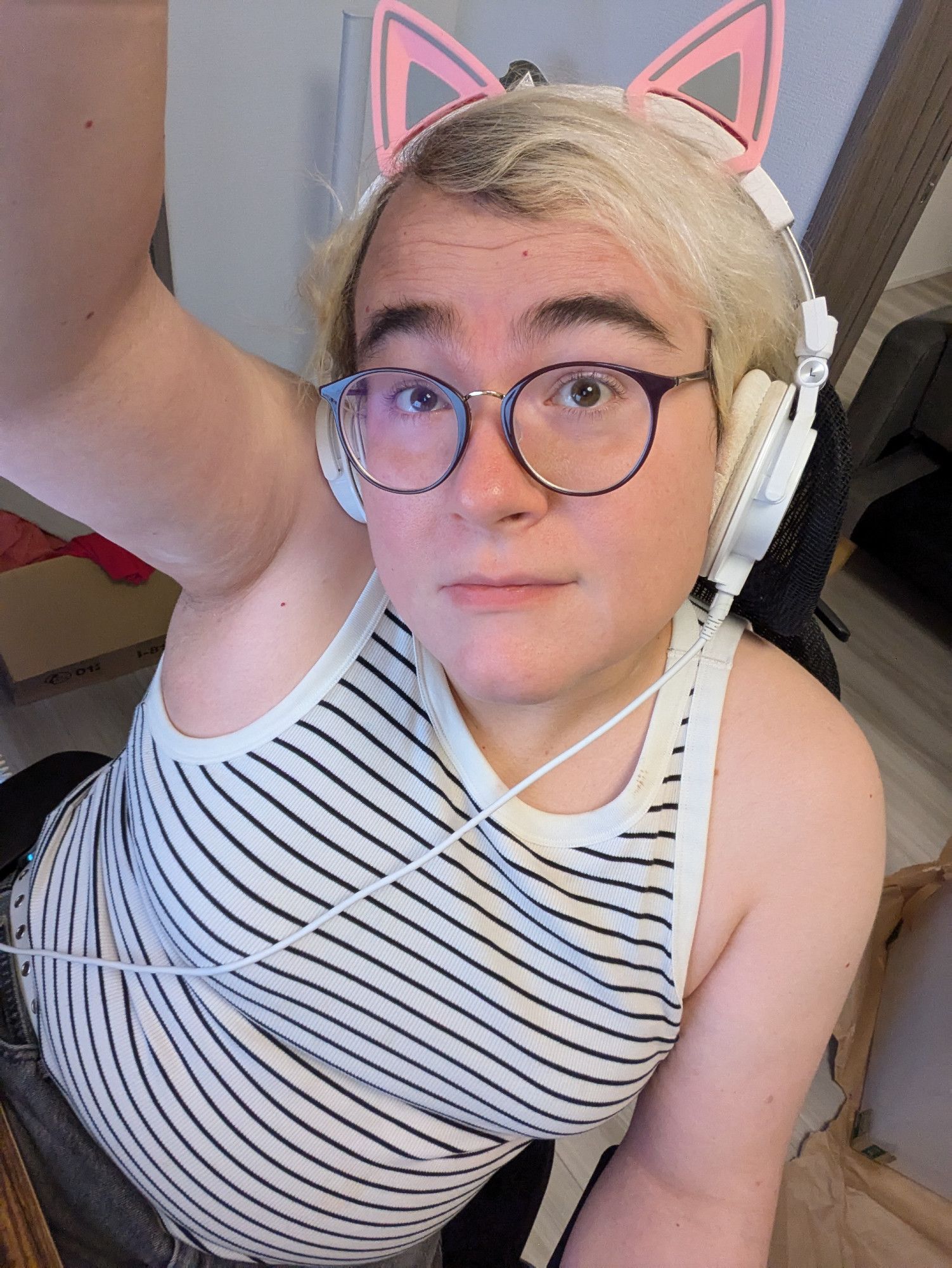 selfie of a trans girl in a tank top, with messy hair and cat-ear headphones