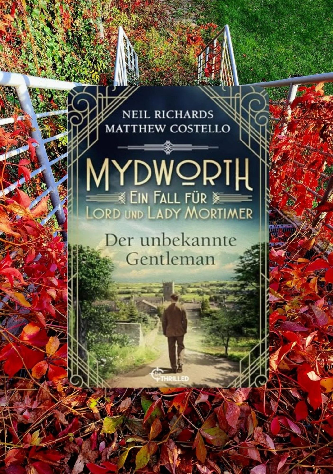 Buchcover von " Der unbekannte gentleman" Aus der Reihe "Mydworth. Ein
Fall für Lord und Lady Mortimer" von Neil Richards und Matthew Costello.  Ist eingefügt in ein Bild mit rotem Herbstlaub und einen metallenen Treppengeländer.