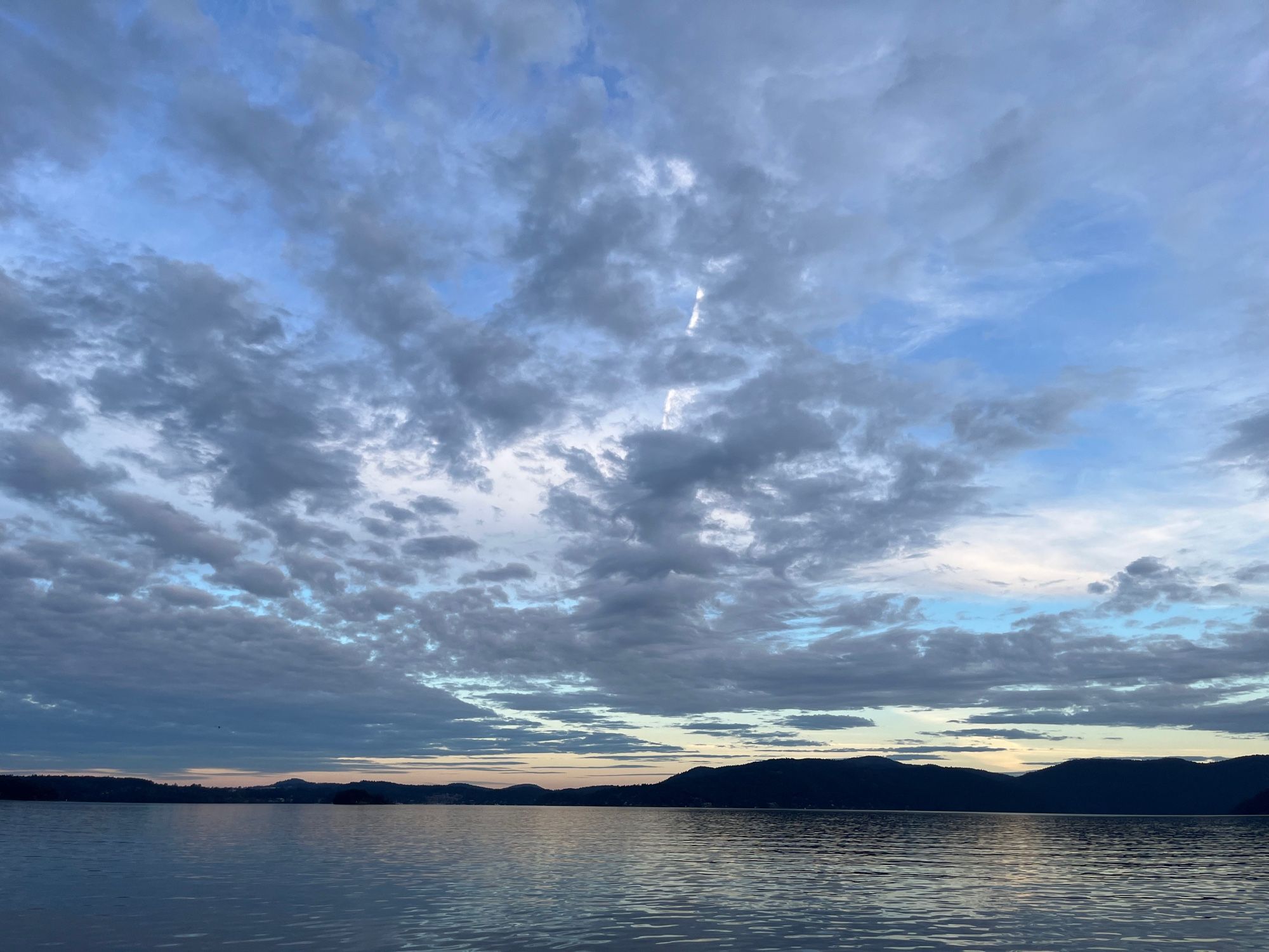 dark shadows of low mountains pressed between glittering gloaming waters and twilight sky with dark grey clouds.