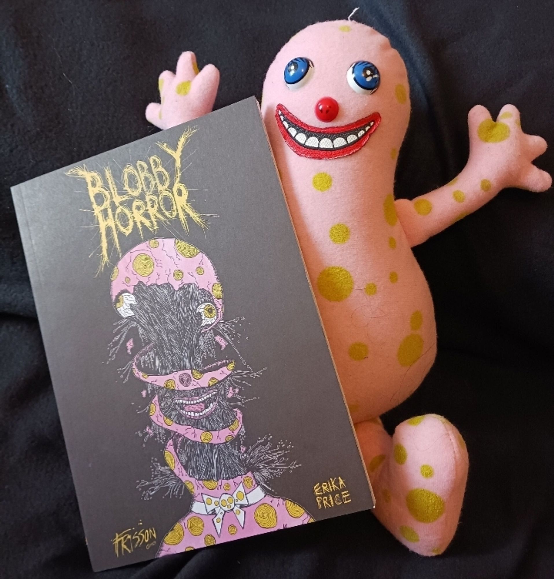 A copy of Blobby Horror, a Mr Blobby anthology put together by Frisson Comics and Erika Price, it is leaning against a horrible Mr Blobby plush