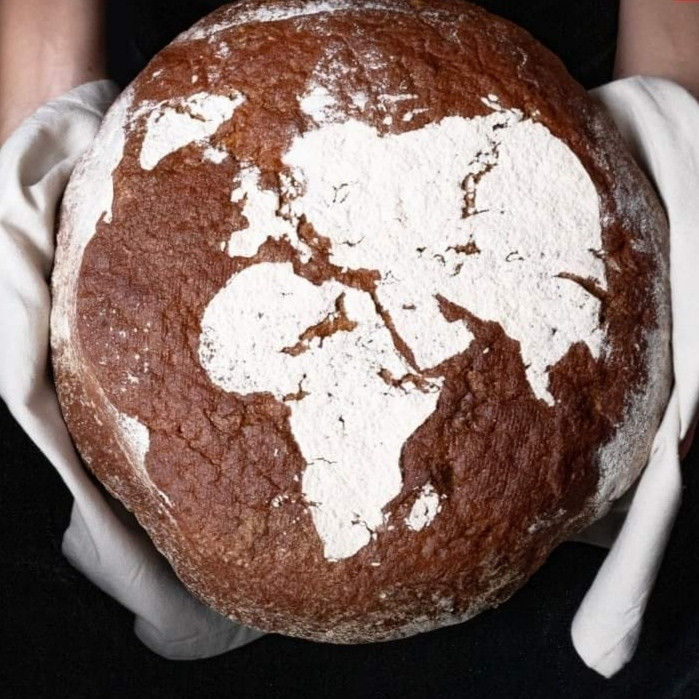 Foto: ein runder Laib Brot. Mit Mehl ist drauf eine Weltkarte gestäubt. Man erkennt Afrika und Eurasien deutlich.