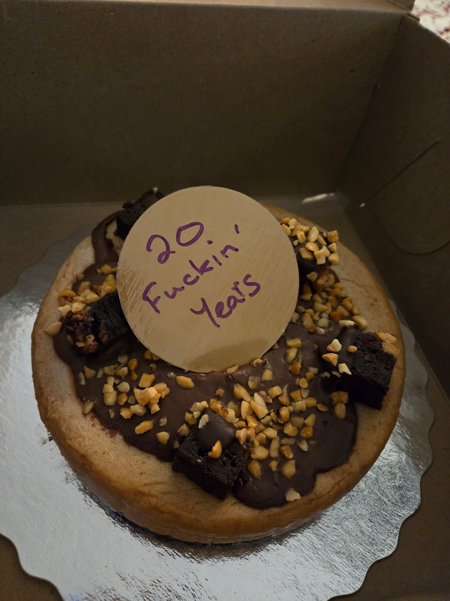 A chocolatey cake with a cardboard topper that says "20 Fuckin Years"