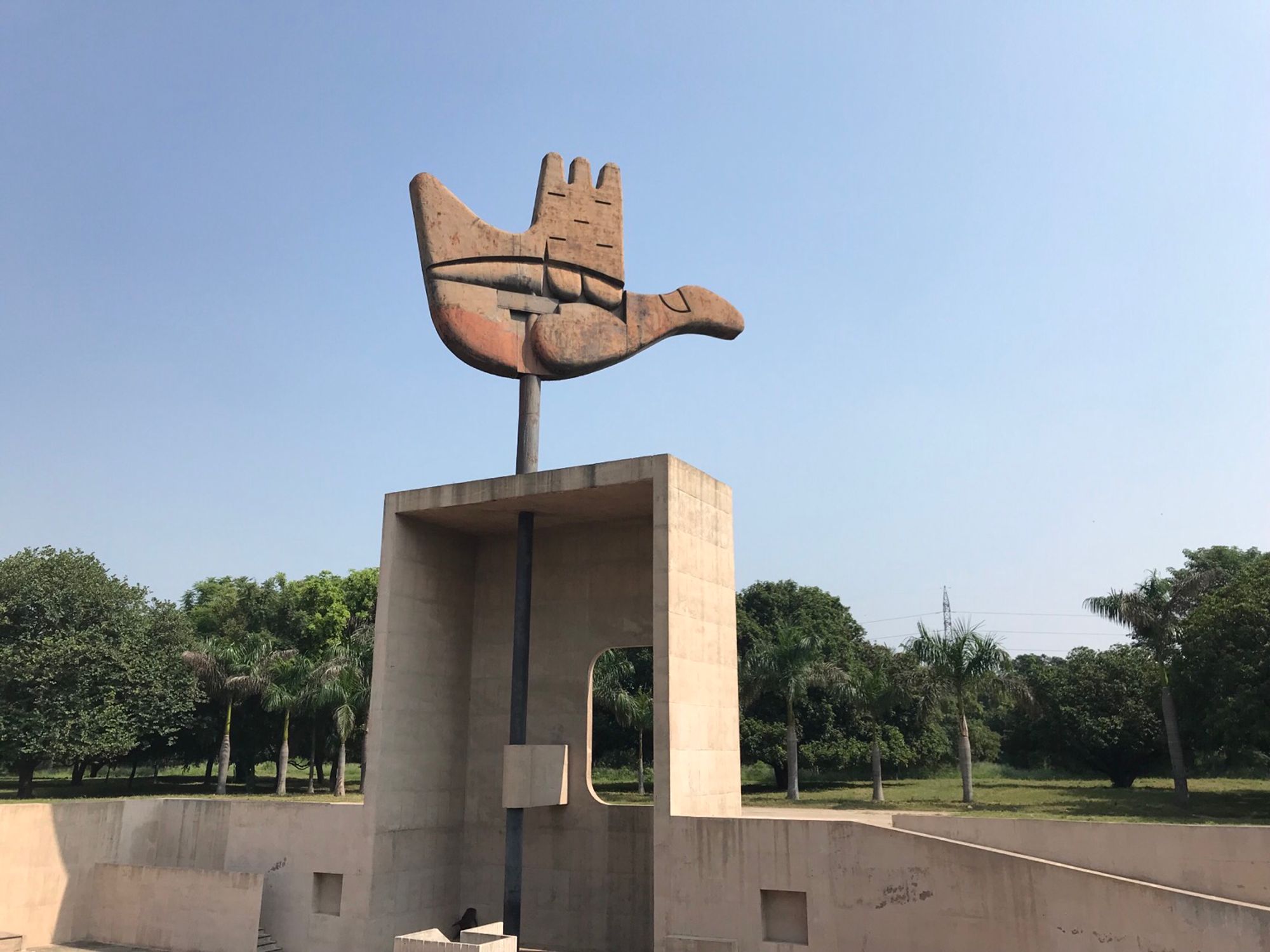 Auf dem Foto ist das Wahrzeichen von Chandigarh, die offene Hand zu sehen. In einem rechteckigen noch vorn hin offenen Betonkasten steckt ein Stahlstab, der am oberen Ende die etwa 14 Meter hohe und etwa 50 Tonnen schwere Hand hält. Die hand kann auch als stilisierte Friedenstaube betrachtet werden. In seiner Gesamtheit ist das Monument etwa 30 Meter hoch und die Hand kann durch den Wind bewegt werden. Es steht für Frieden.