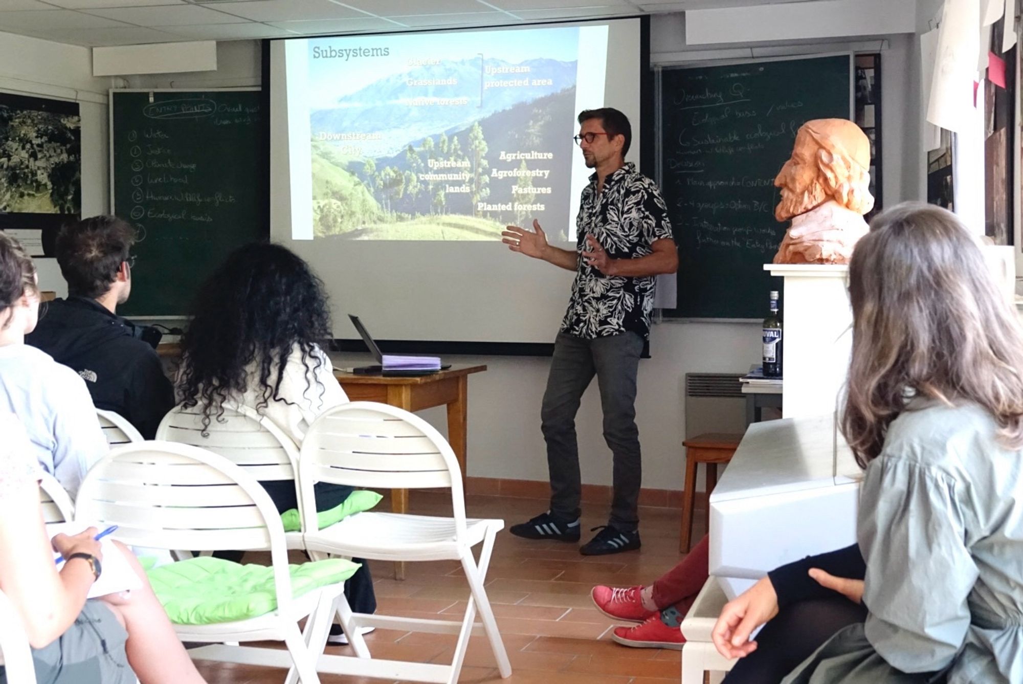 Bruno Locatelli speaking in the lecture theatre in Peyresq, some students, a piano and a bust of the head Nicolas-Claude Fabri de Peiresc